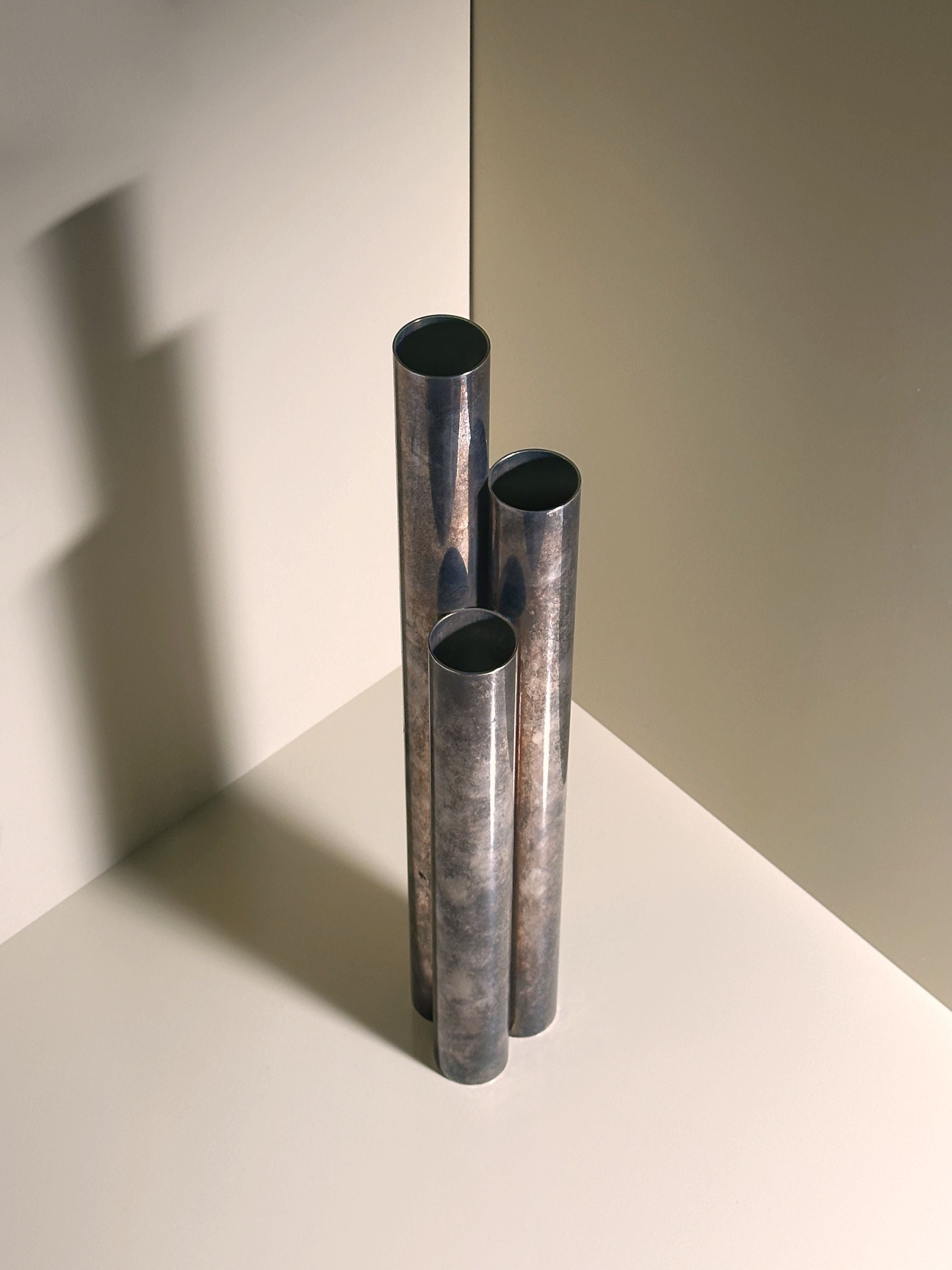 Three Silver-plated Tall Brutalist Vases by Dodo Vintage, designed by Gio Ponti Italia in the 1960s, stand on a light surface. The lighting casts soft shadows to the left, highlighting their sleek, textured finish and classic design.