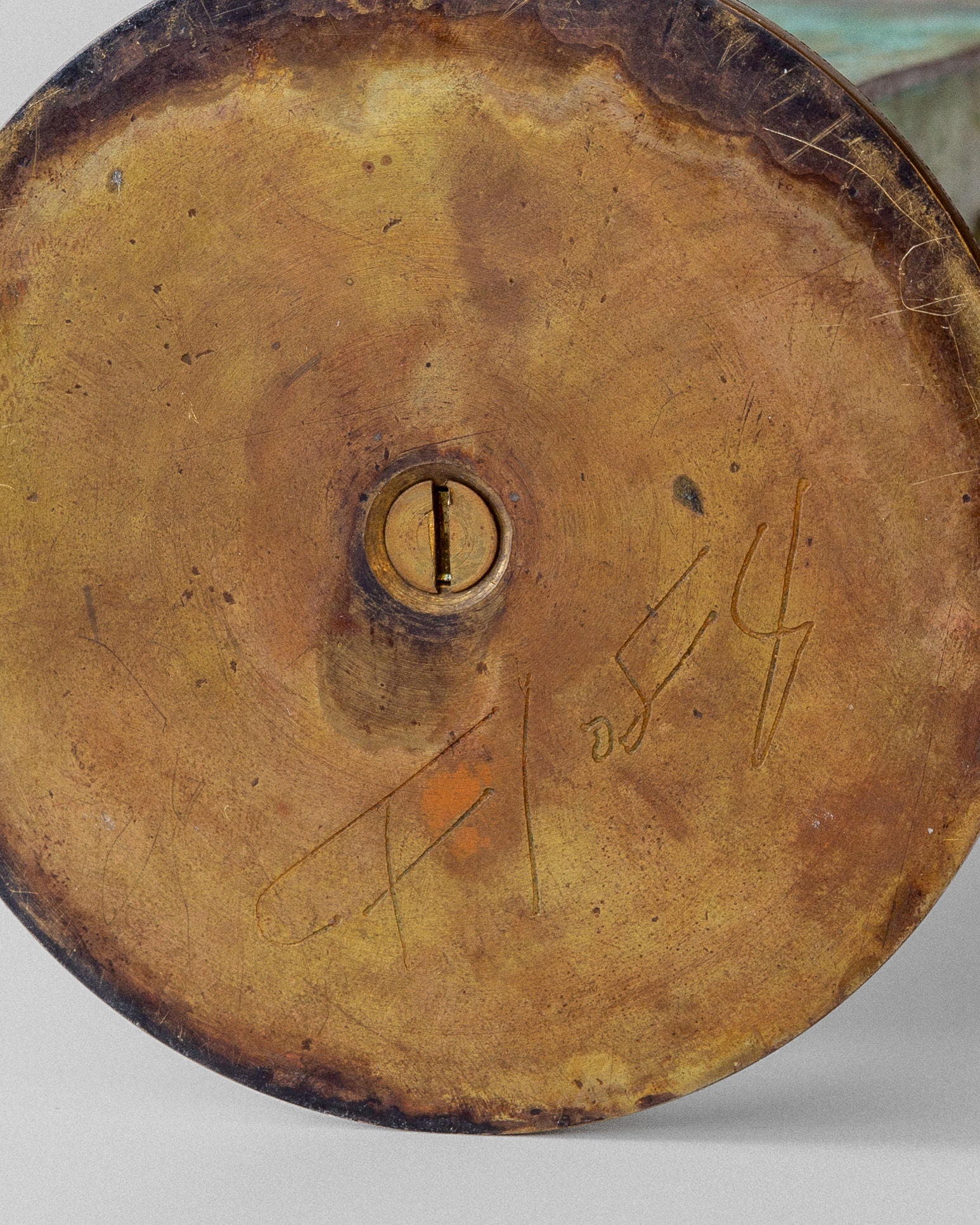 Close-up of the round base of the Spigel Art Deco Brass Vase, featuring a central screw and engraved inscription. Signs of wear and verdigris patina at the edges suggest its Swedish origin.