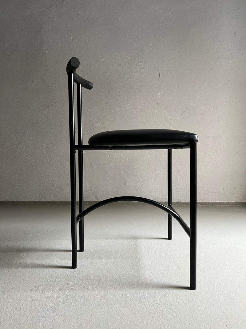 A set of 4 Postmodern "Tokyo" Chairs by Rodney Kinsman, available from Veter Vintage, are shown against a plain, light-colored wall. These chairs feature round cushioned seats in faux leather upholstery, slender legs, and slightly curved backrests with horizontal bars for support. Shadows are visible on the floor.