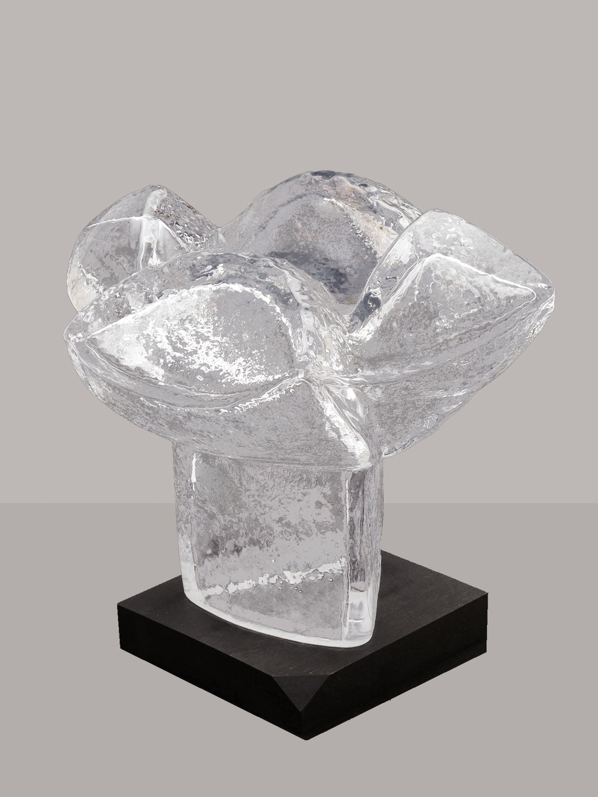 On display on a black rectangular base is the Very Large Abstract Glass Sculpture by RELIC LONDON, a clear glass piece with an elegant curved, flower-like shape. The surface boasts a textured design with small bubbles and imperfections, creating an intricate look. This exquisite Swedish-made sculpture is perfect for any art collector and stands out against a plain gray background.