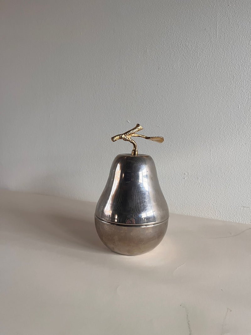 The Maud Vaughan Mid Century Pear Lidded Box, crafted as a silver container with a gold stem, elegantly rests on a smooth surface against a plain white background.