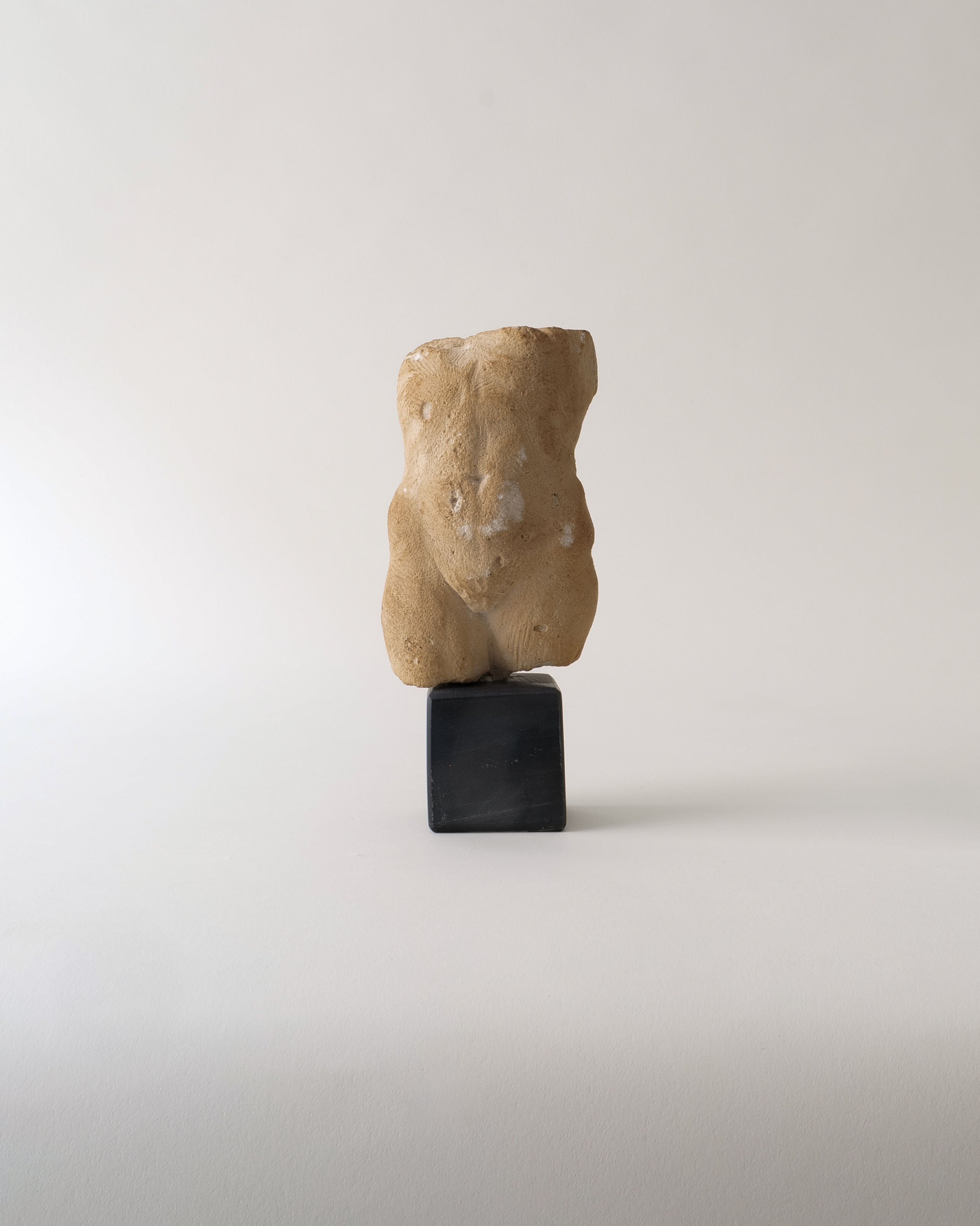 The "Torso Sculpture" by Misja Kristoffer Rasmussen (b.1971) for Collection apart features a weathered beige human torso, reminiscent of classical sculpture, displayed on a dark pedestal against a plain light background.