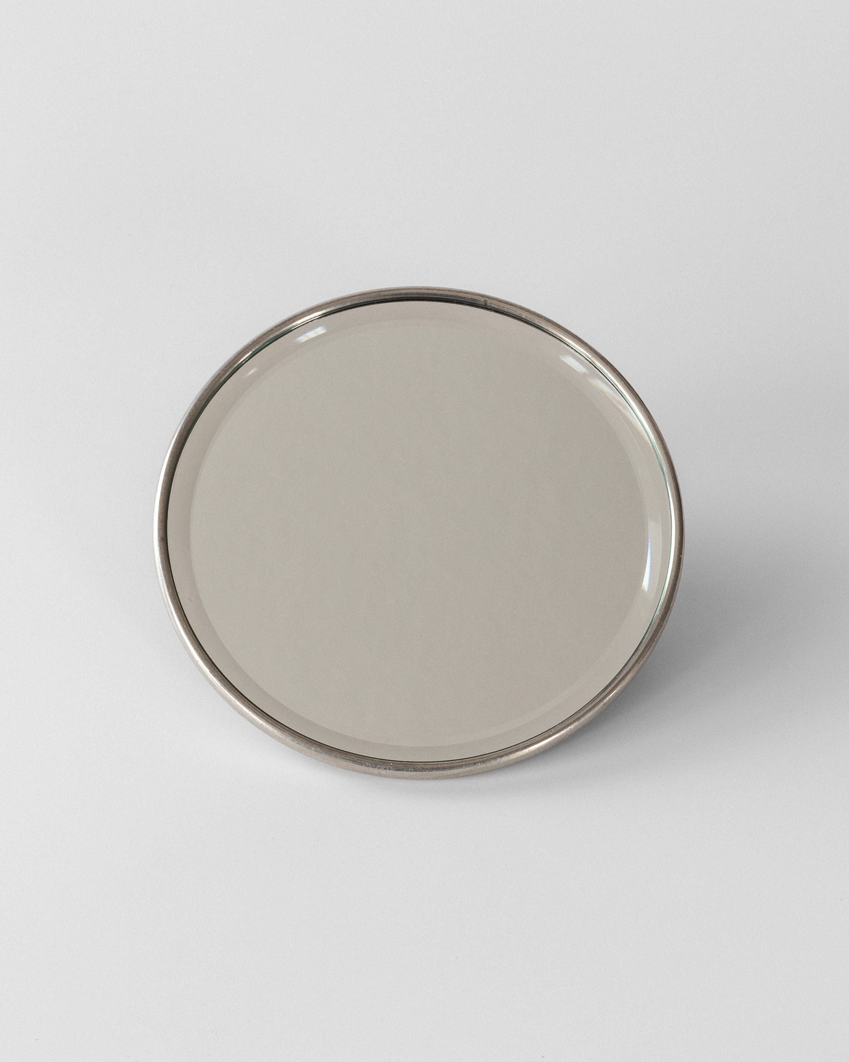 A plain, round, beige ceramic plate with a glossy finish sits against a neutral gray background. Its minimalist design and slightly raised rim evoke the subtle sophistication of Swedish Grace, reminiscent of Spigel's Art Deco style seen in their Metal Mirror with Koi Fish from the 1920s.