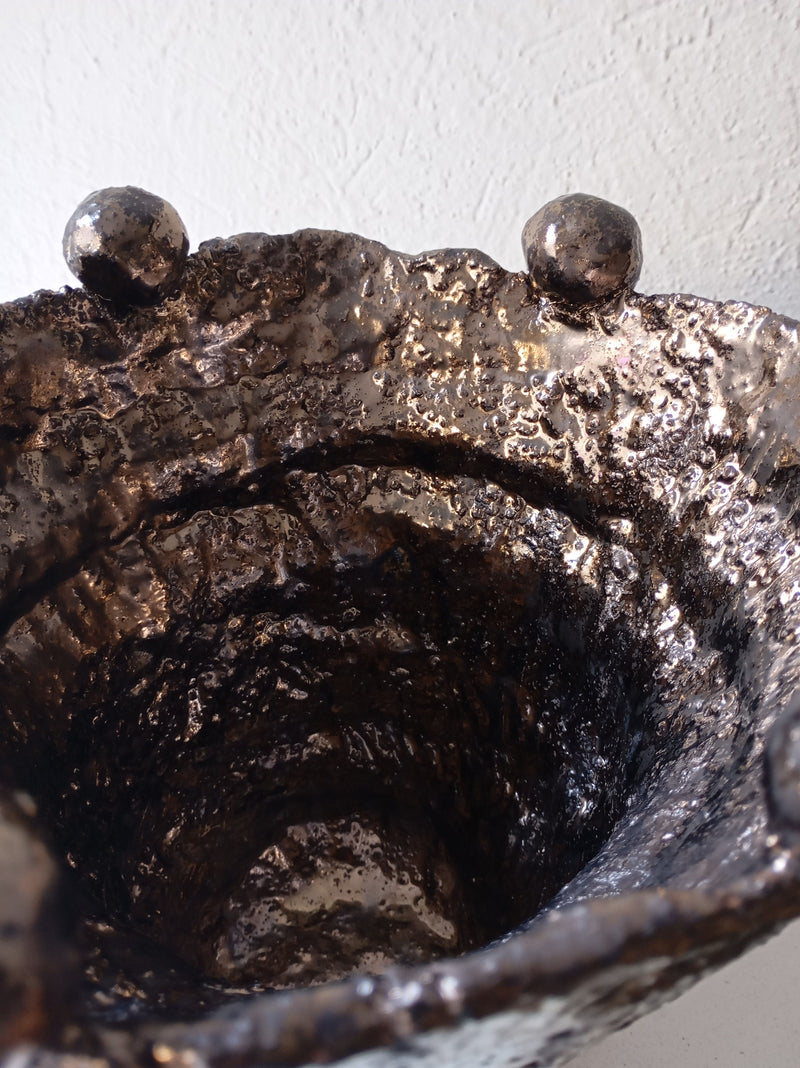 A close-up of the Coupe Lilibeth 3 by Claire Pain, a unique bronze enamel stoneware bowl featuring three rounded knobs on its irregular rim, set against a light textured background.