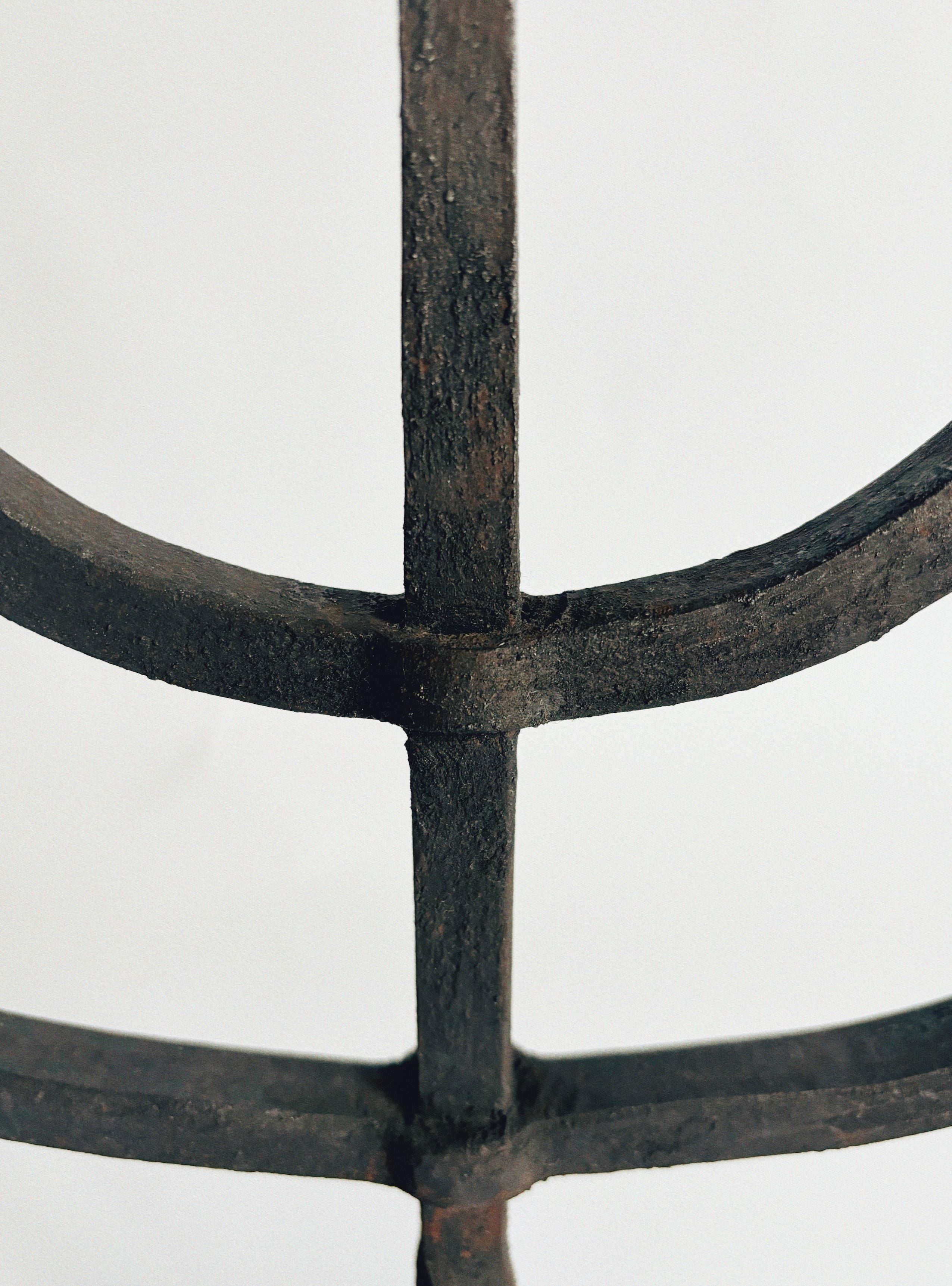 Close-up of the Hand Forged Candleholder by Huerto, showcasing a rustic, weathered wrought iron design with intersecting vertical and horizontal bars that form a grid-like pattern against a plain background. The metal features an aged appearance with a textured, dark brown surface.