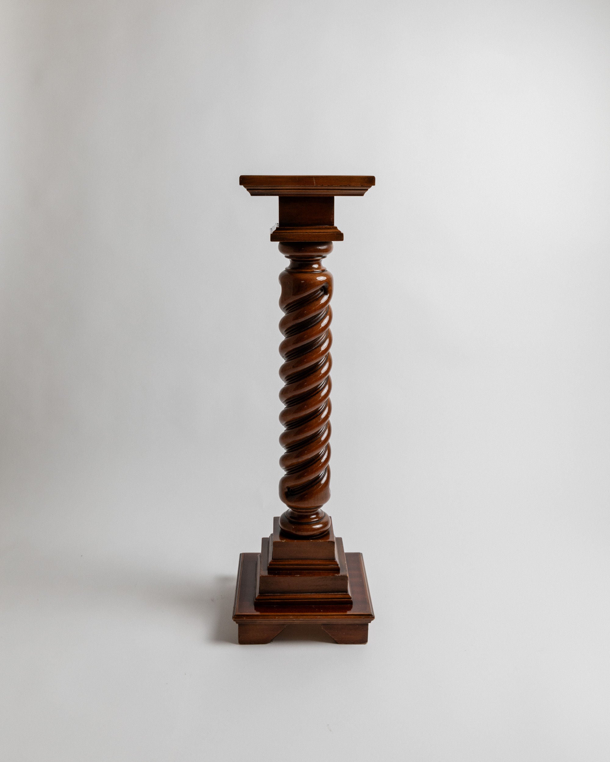 The Bottega Jacobs 'Wooden stand, Italy 1960s' is a vintage piece with a spiraled column design on a pedestal, handcrafted in solid wood featuring a polished dark finish against a light background.