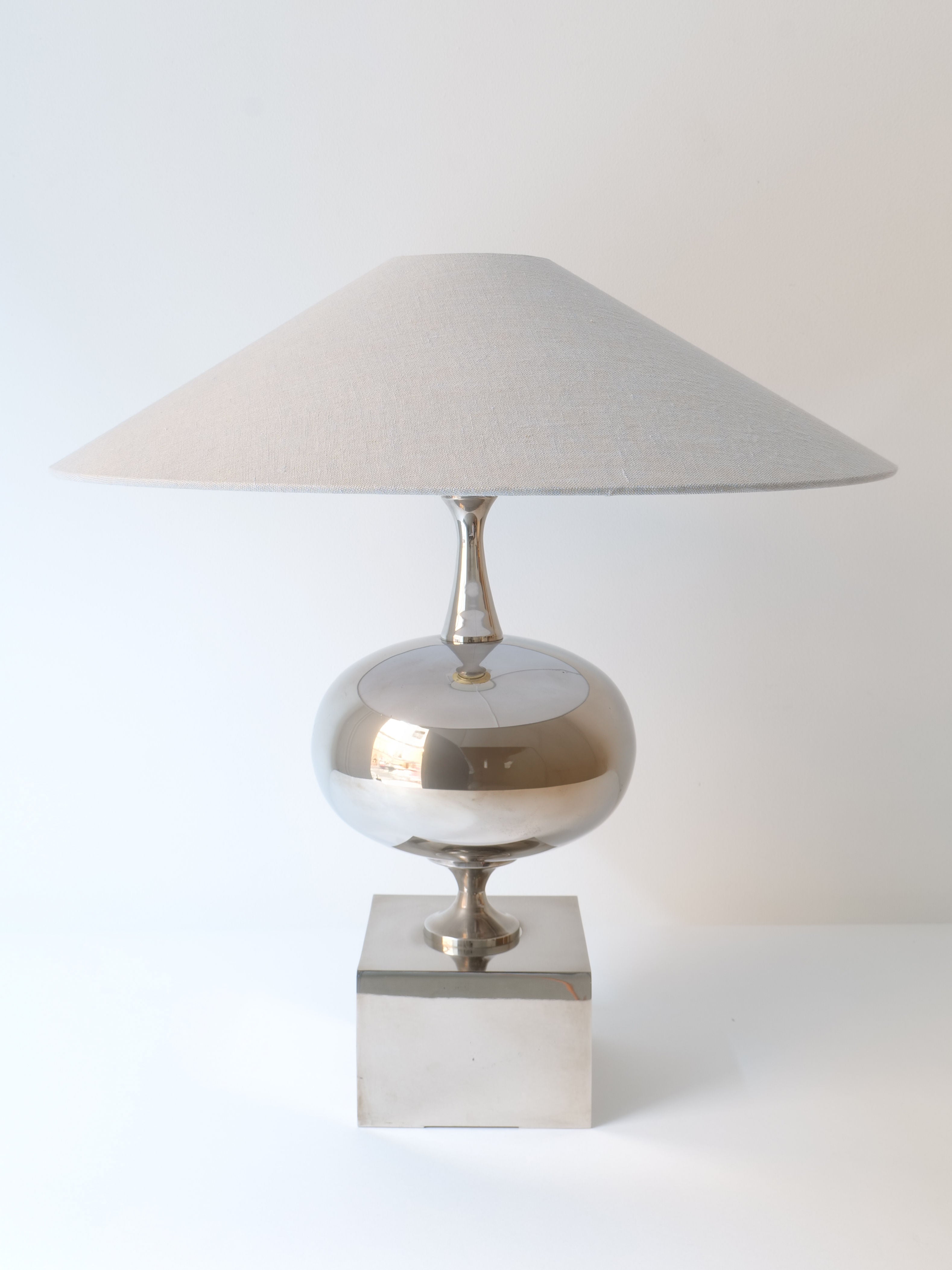 The Barbier Sculptural Lamp 1970s by Collection apart features a modern design reminiscent of 1970s French lighting, with a metallic spherical base and a square bottom on a white surface. It is topped with a large, conical beige lampshade and boasts sleek, minimalist lines, making it perfect for contemporary interiors inspired by classic Philippe Barbier table lamps.