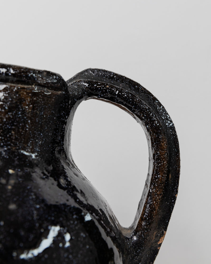Close-up of a textured handle from Bottega Jacobs' Antique Terracotta Jug - Italy 19th Century, featuring a vintage design. The surface is glossy with a speckled white and black pattern that beautifully reflects light, set against a plain white background.