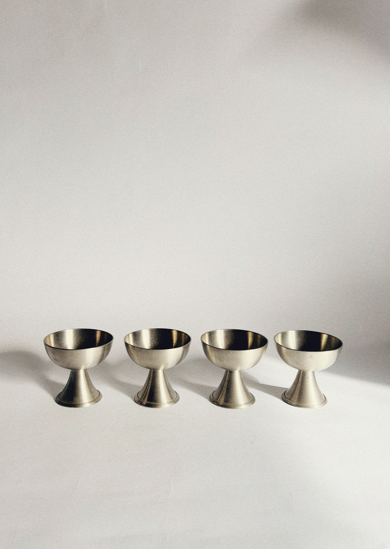 Set of four brushed brass dessert coupes on white surface