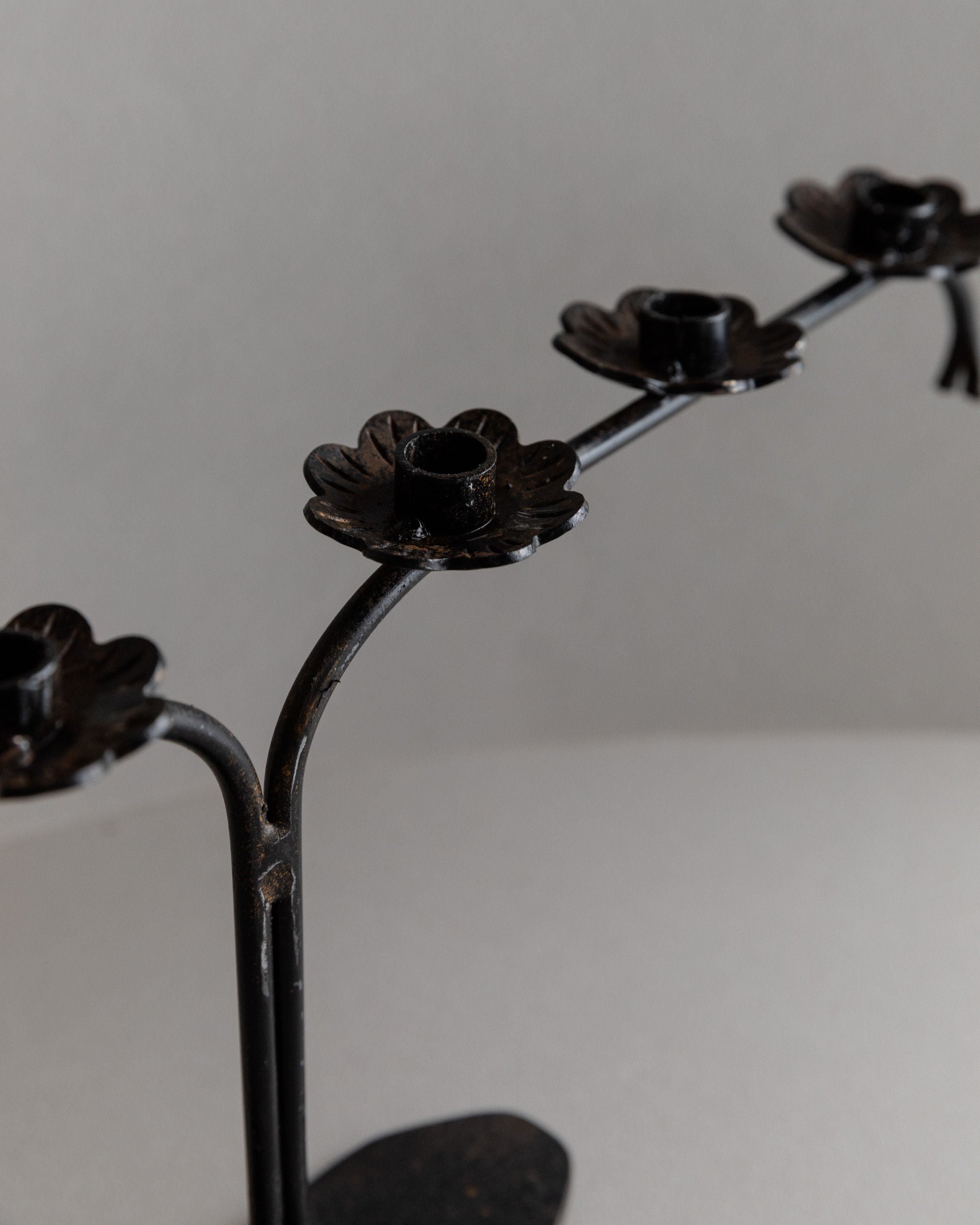 A close-up of the Bottega Jacobs Iron Candleholder, Italy 1960s, crafted from black metal with flower-shaped platforms and brutalist design elements against a neutral gray background, making it an eye-catching table decoration.