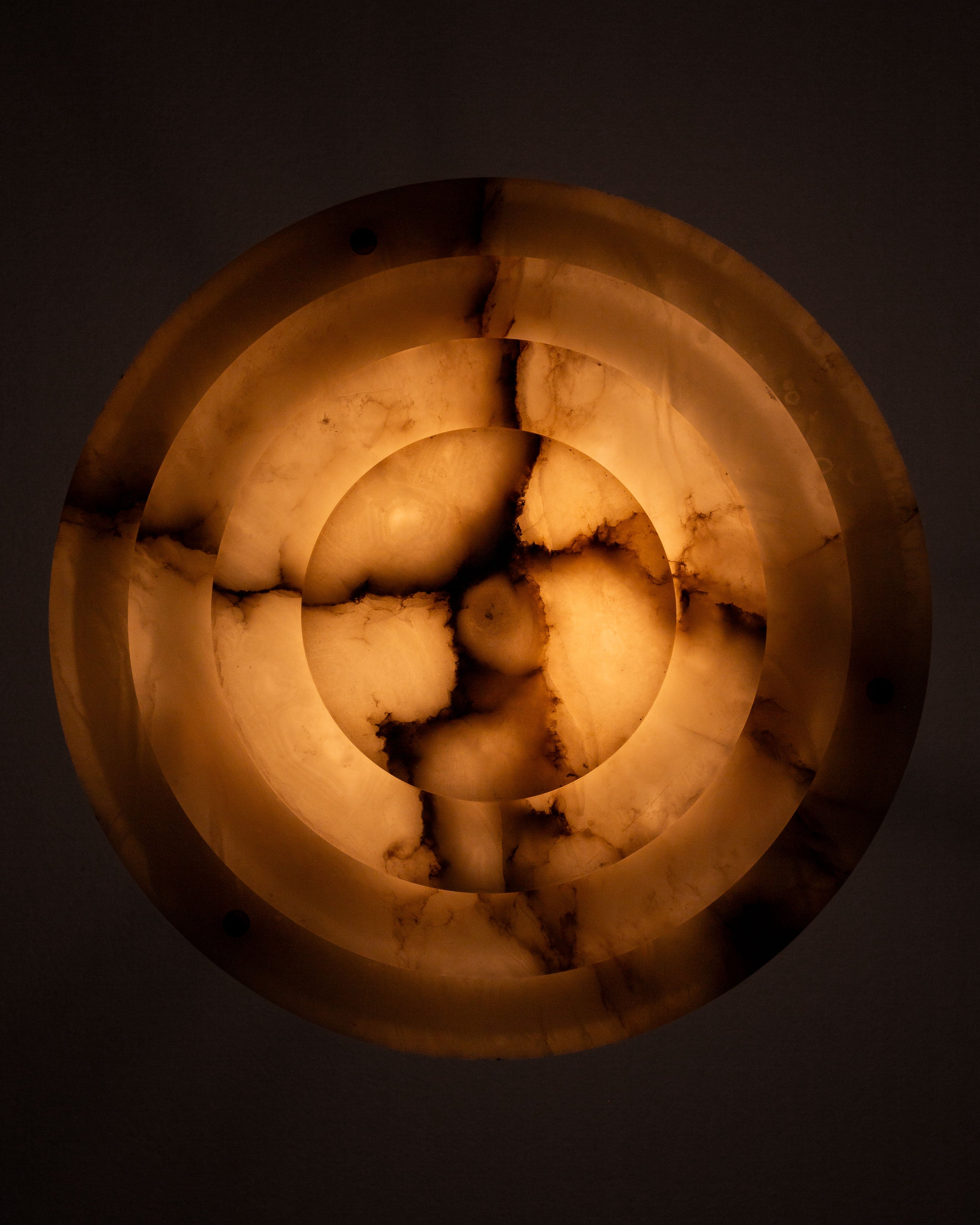 The Spigel Art Deco Alabaster Pendant Chandelier emits a warm, amber glow with a marbled pattern and concentric circles featuring darker veining, offering soft, diffused illumination.