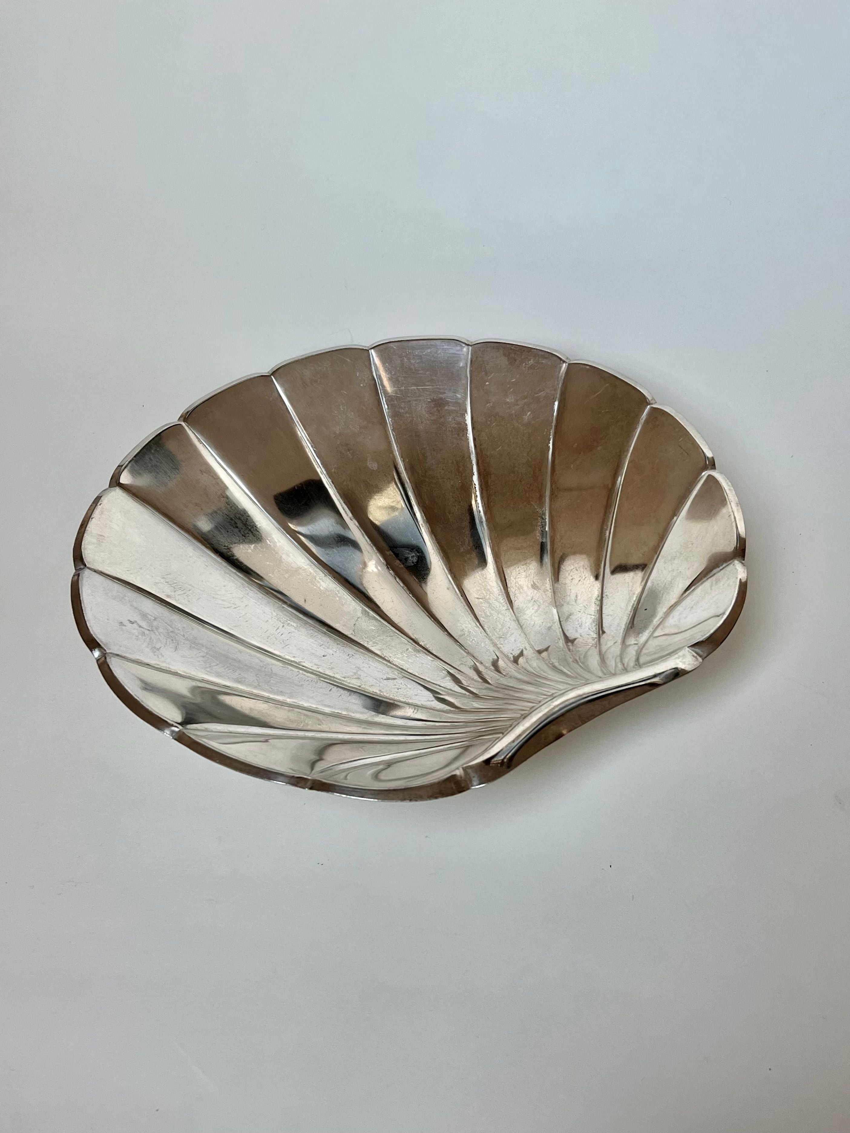 The Grand Silver Shell Dish by Manushi, sourced in France, features a polished, reflective surface with scallop-like ridged segments. Elegantly displayed against a plain white background, it beautifully embodies simplicity and sophistication.