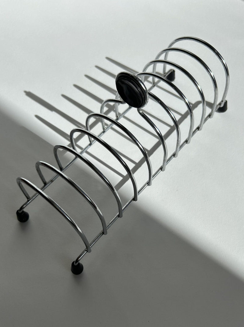 A Postmodern Toast Rack by Flock Studio, featuring vertical slots, casts striking shadows on a white surface. The light angle highlights its distinctive 1950s design aesthetic, reminiscent of Tomado Holland's creative flair in toast rack design.