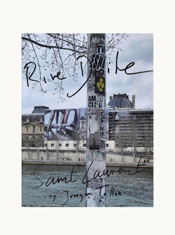 A photograph of a river with a pole covered in stickers in the foreground. In the background, a large building is visible, partially obscured by scaffolding. Handwritten text on the image reads "Maison Plage System Magazine Issue No. 13 by Juergen Teller," reminiscent of an editorial piece from System magazine.