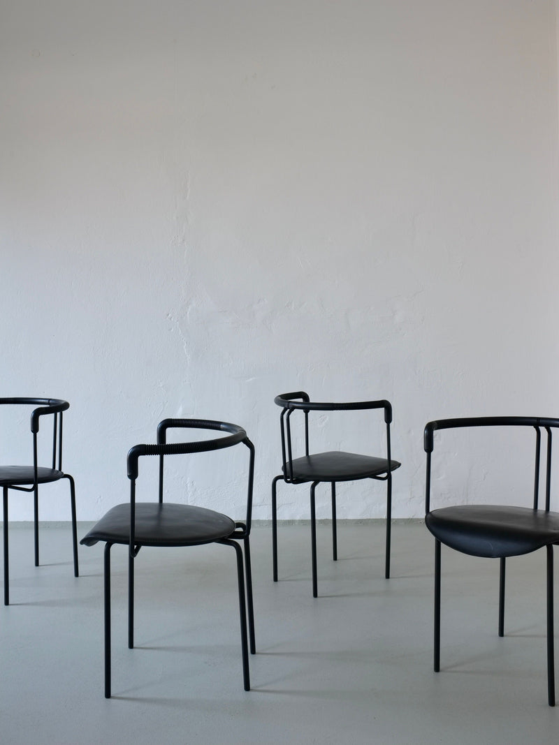 Four black leather postmodern armchairs arranged on concrete floor