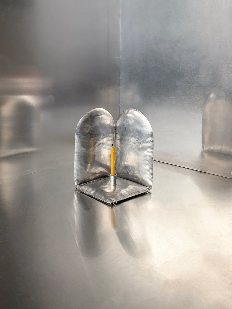 The Phaedra candle holder ALTAR by Bregje Sliepenbeek is a sleek, minimalist metal menorah with two curved panels and a beeswax candle in the center. Hand-made in Amsterdam, it creates an industrial, modern ambiance with its soft reflections.