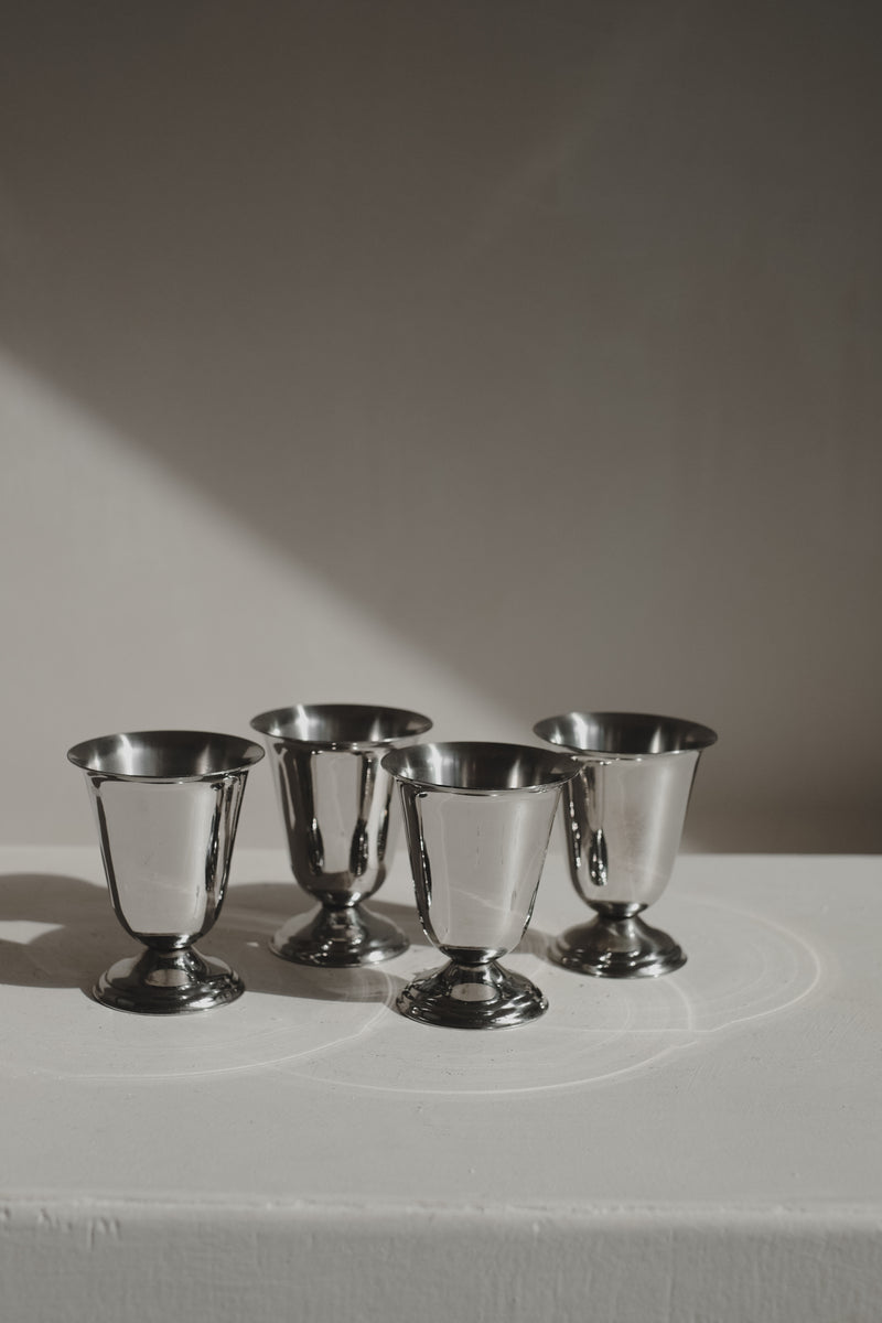 A Set of 4 Coupes by Guy Degrenne, offered by septembre studios, are displayed in two rows on a white surface, where soft natural light creates elegant shadows and reflections on a neutral background.
