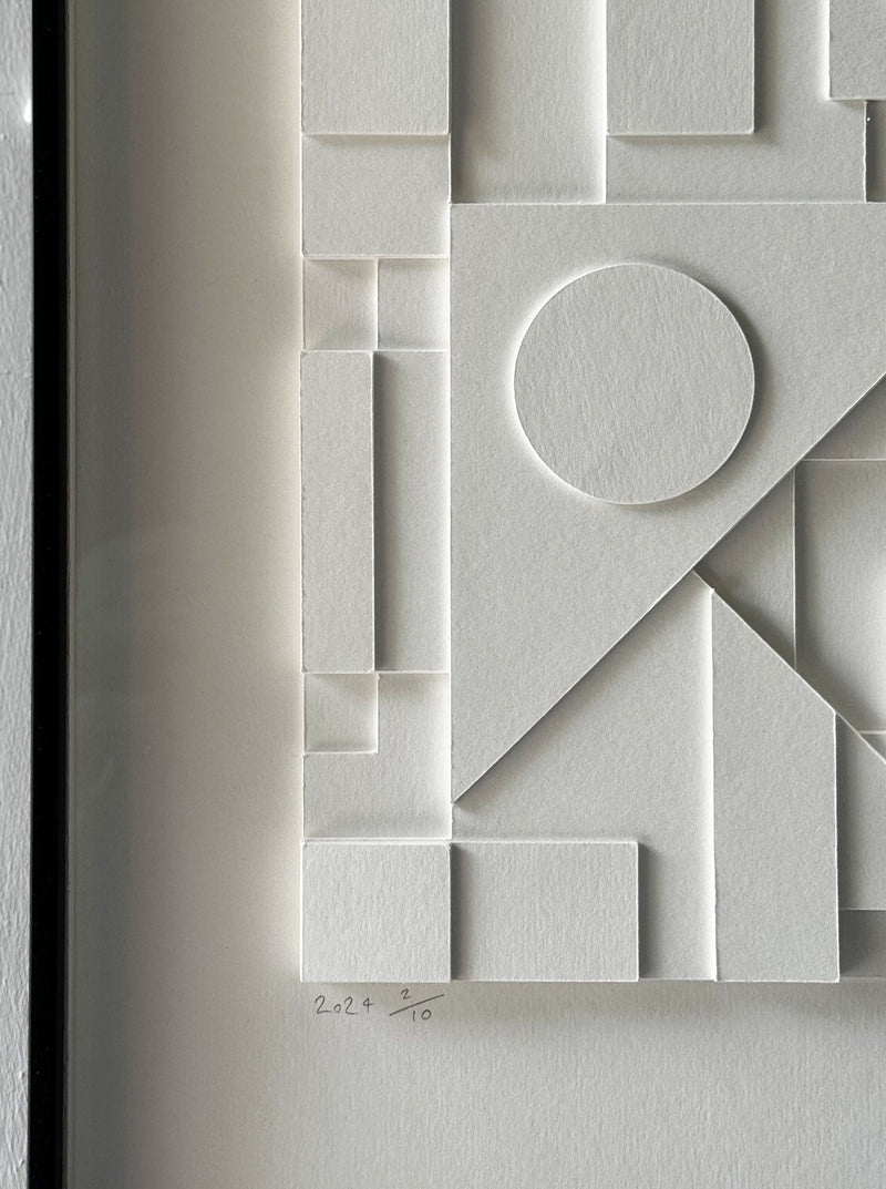 Close-up of a white framed abstract artwork, showcasing various raised geometric shapes including circles, triangles, and rectangles, creating a textured pattern. This handmade paper relief is a limited edition piece by Sean Thornhill, with the bottom left corner signed "22/220." The product name is Composition124.