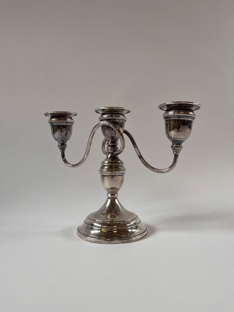 The Maud Vaughan Vintage Silver Plate Candelabra features intricate detailing with three elegantly curved arms and a rounded base, set against a plain gray background.