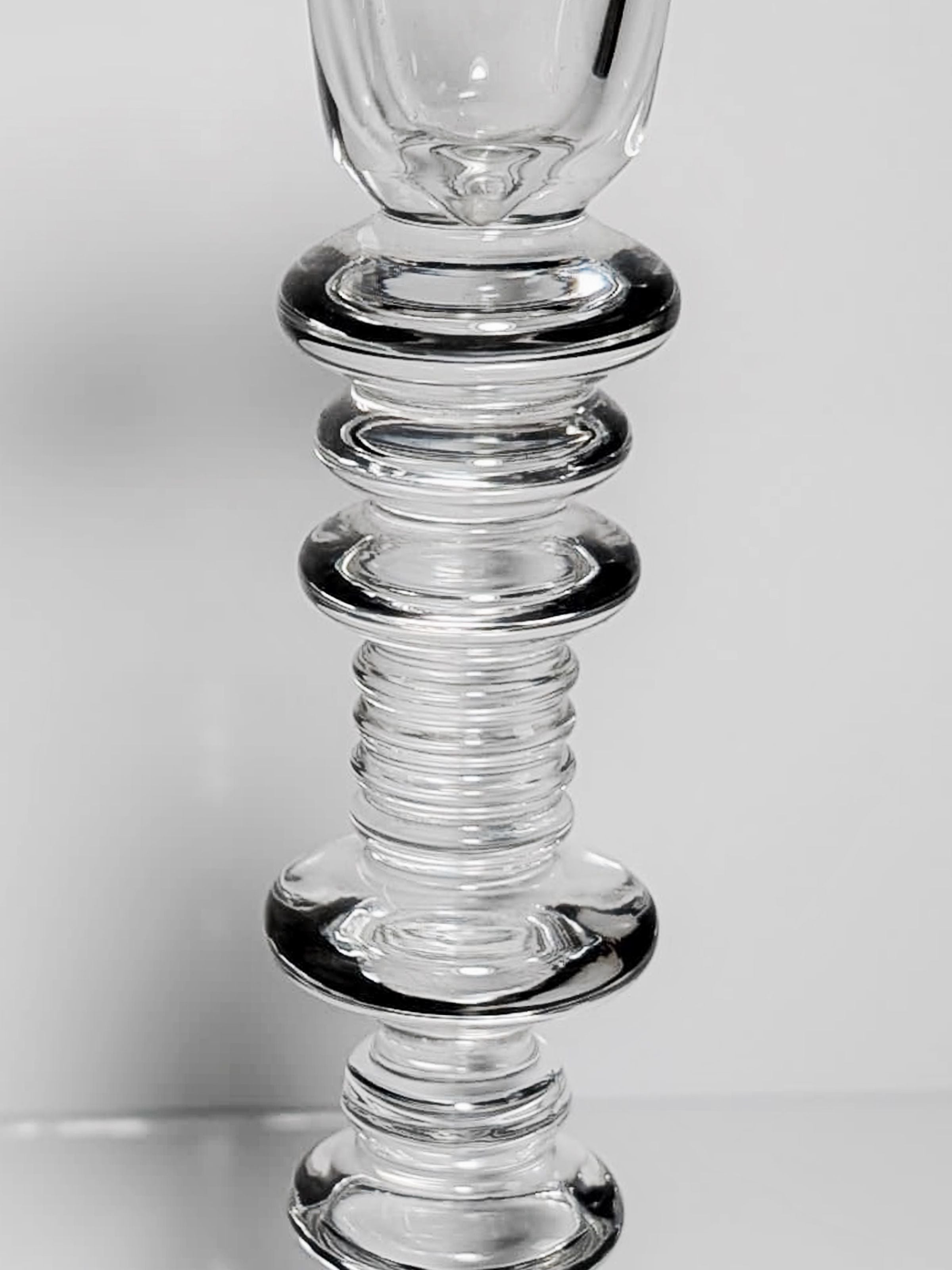 Close-up of a mid-century glass object with stacked, circular, and ribbed sections, resembling one of the Set of 2 Glass Candleholders by Peill & Putzler from Dodo Vintage, against a plain gray background.