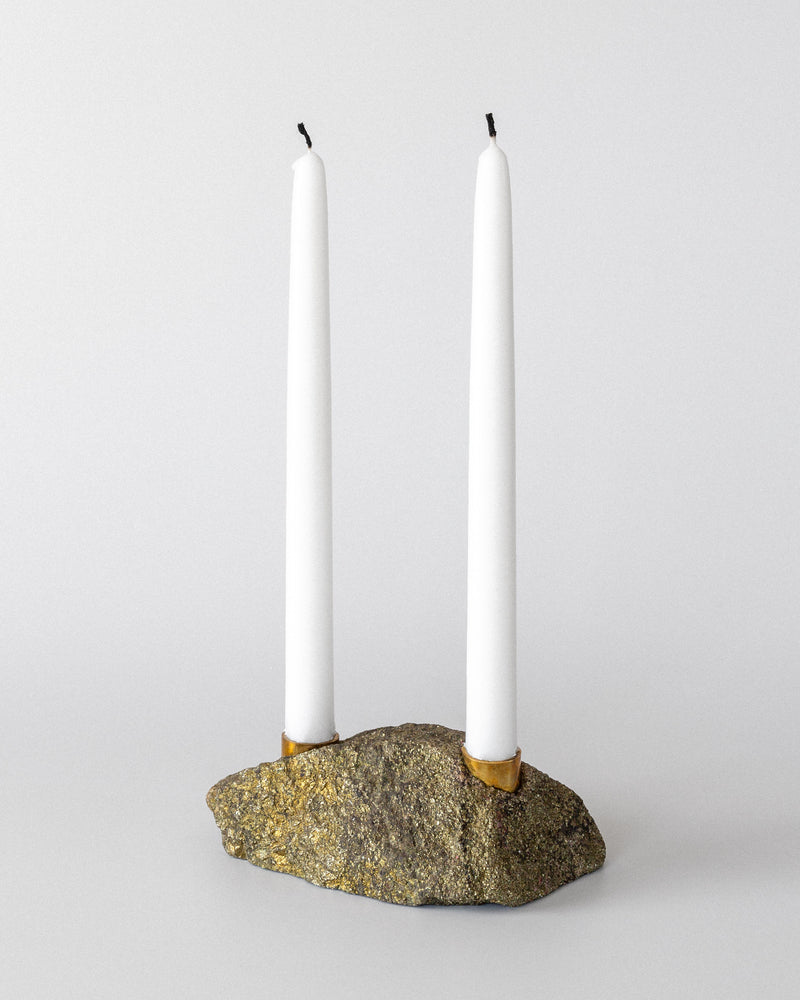 Two white taper candles are displayed in the 1970s Spigel Brutalist Stone and Brass Candleholder, featuring a roughly textured, oval stone base, set against a plain white background.