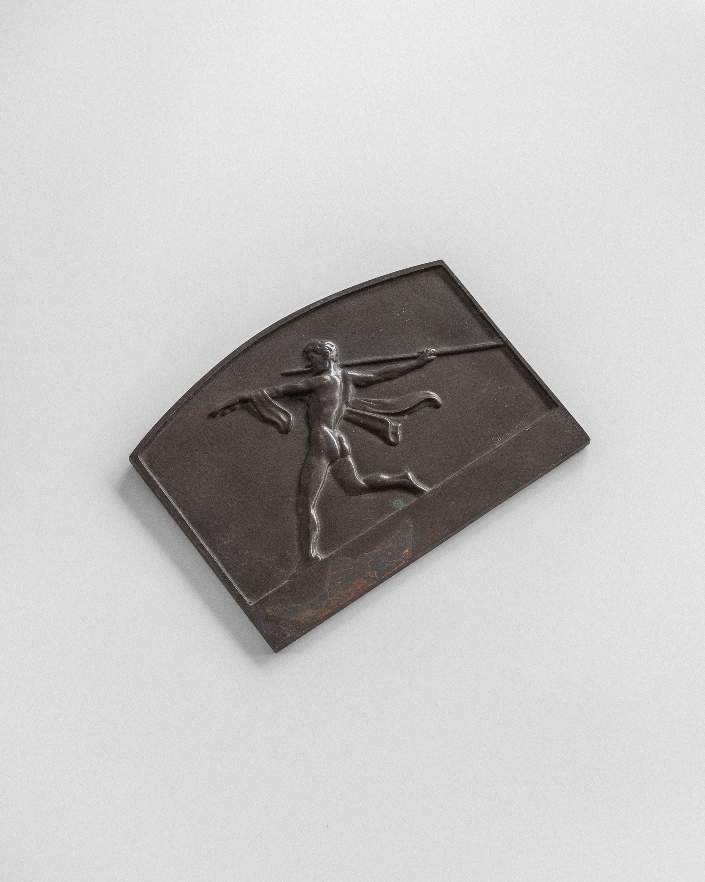 The Art Deco Bronze Wall Relief by Spigel is a bronze rectangular plaque showcasing an athlete in motion with a javelin. The dynamic figure stands against a plain background, merging classical imagery with subtle Art Deco influences.