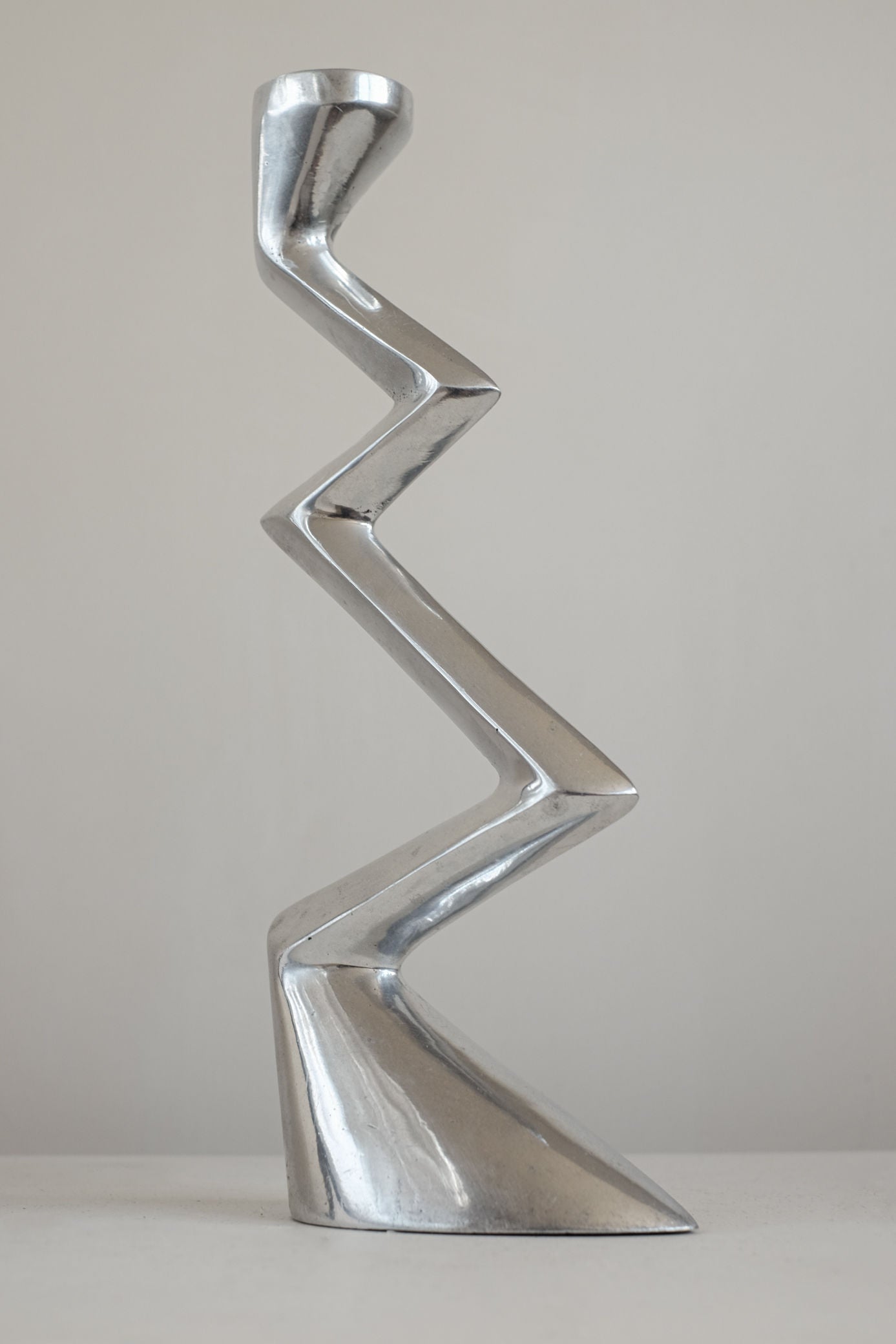 The Matthew Hilton ZigZag Candle Holder Large by septembre studios features a modern, silver-toned angular design—ideal for contemporary interiors and shown against a light background.