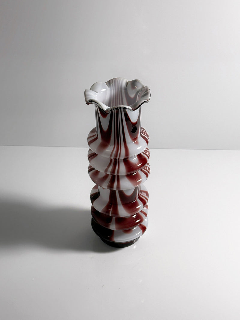 A 1970s Carlo Moretti Opalina Fiorentina vase from Dodo Vintage, with a fluted rim and red-and-white swirls, sits on a white surface against a light gray background.