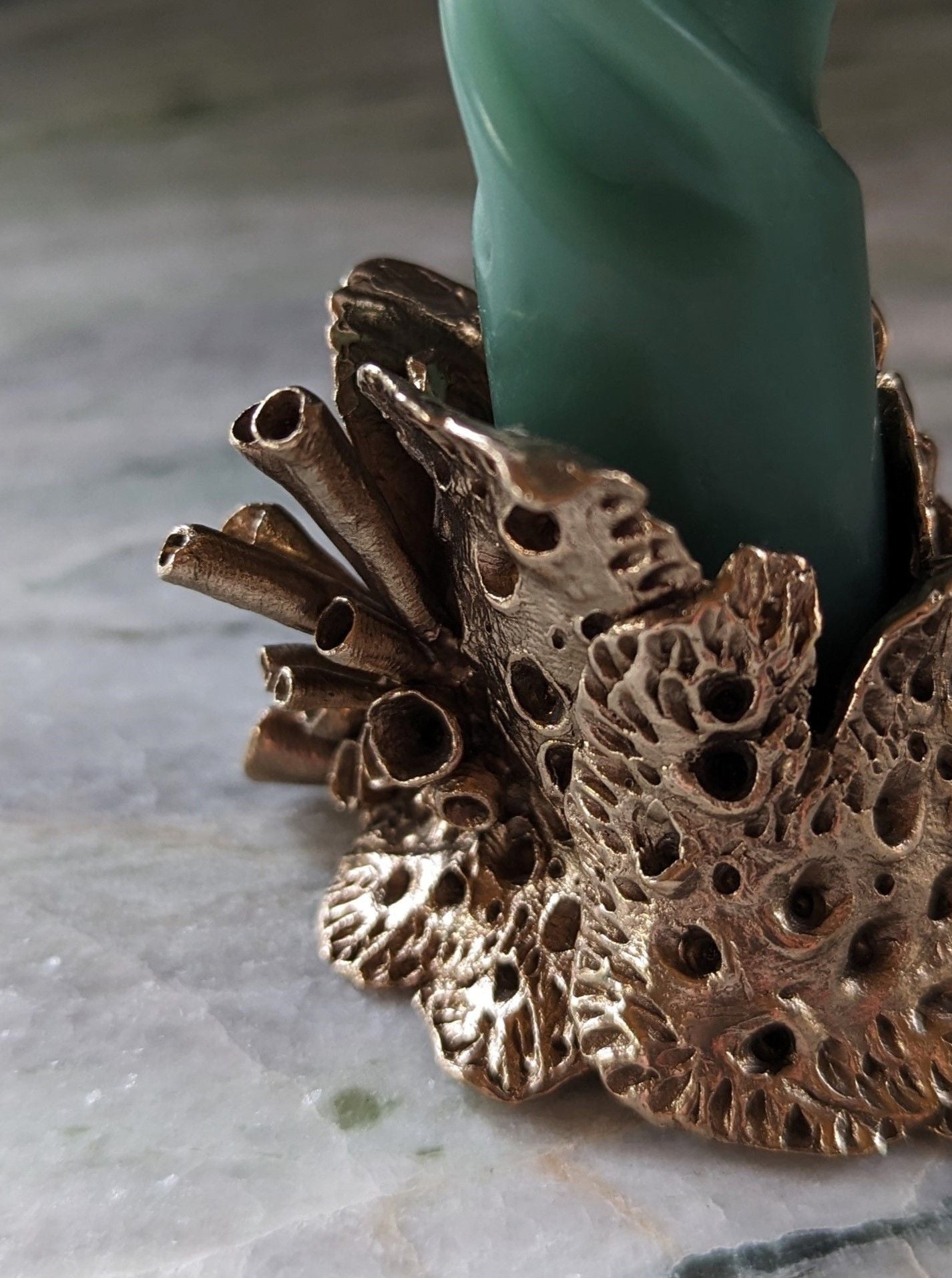 A close-up photo of a Sophie Symes Bronze Lichen Candle Holder with a decorative organic bronze base designed to resemble textured leaves, showcasing intricate details and craftsmanship.