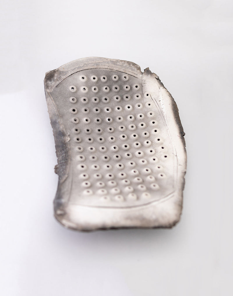 The silver metal grater, featuring a rectangular shape with rounded edges, sits elegantly much like the Two Freeform Raku Platters by John Dunn from RELIC LONDON. Its array of small circular holes and gently worn edges add inviting texture against a plain white background.