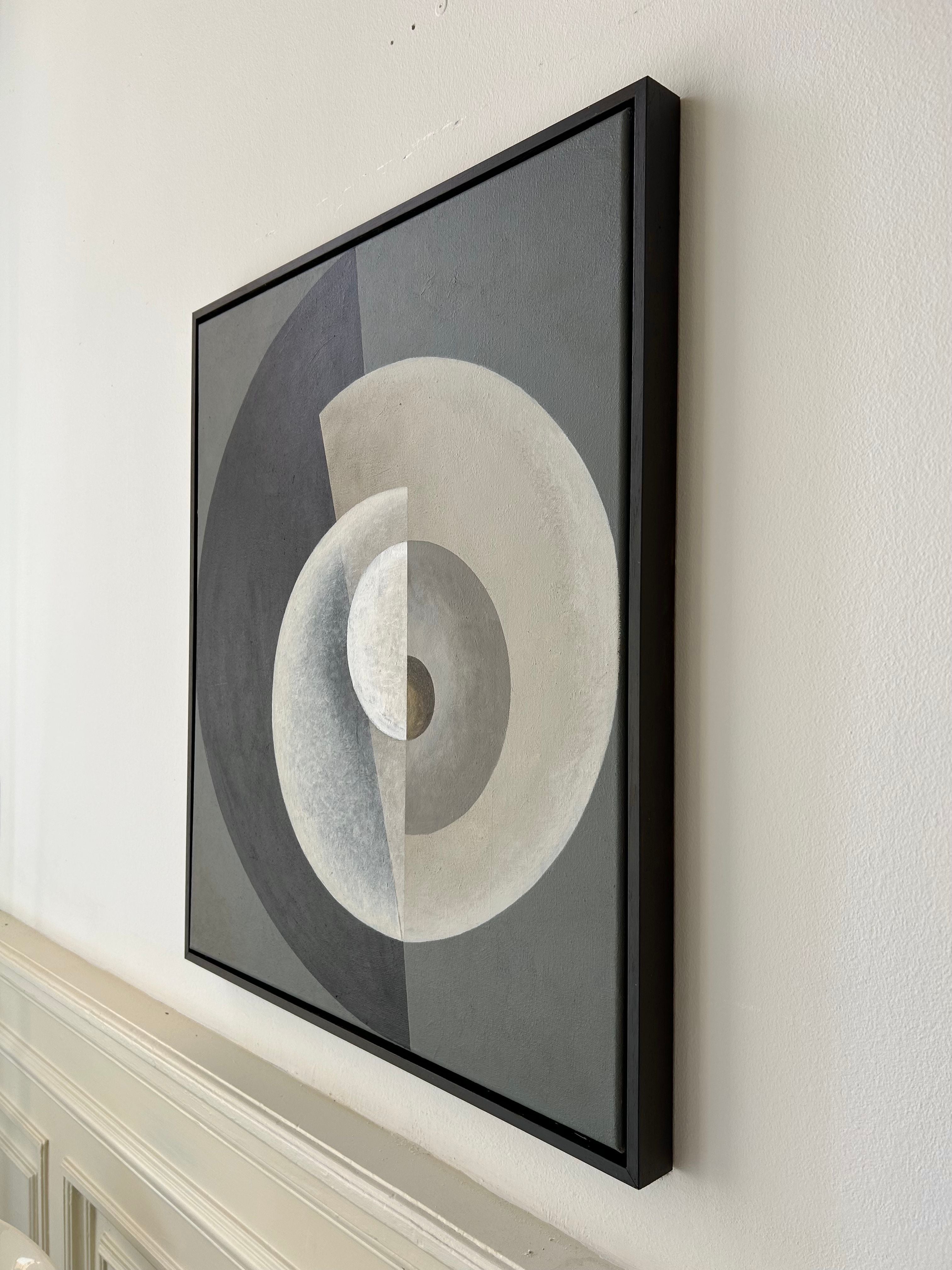 A framed abstract painting in a brown wooden box frame features a composition of overlapping circular and semi-circular shapes in varying shades of gray, white, and black. The acrylic on canvas artwork is mounted on a light-colored wall above a panel of molding or wainscoting. "Spiralling" Painting, 2024 by Iris Bavelaar