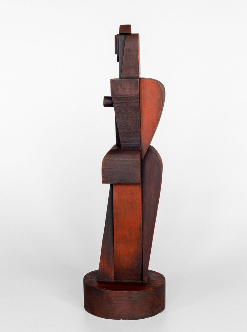 A side view of the Cubist Sculpture by Spigel, showcasing abstract, cubism-inspired block-like shapes that form a stylized human figure. The wooden sculpture is finished in a dark brown hue and stands on a circular base against a plain white background.