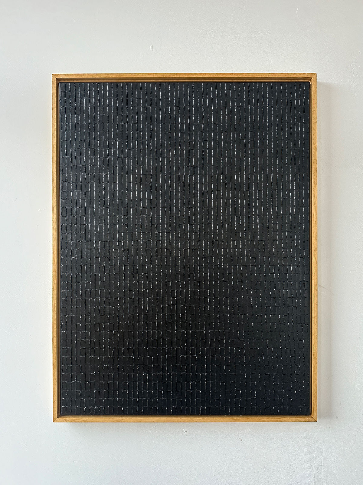 The "Lamp Black" oil on canvas painting by Roi Elmaliah is framed in a simple wooden frame, evoking Amsterdam's minimalist art style, and displayed on a plain white wall. The surface of the artwork showcases a grid of subtle vertical lines.