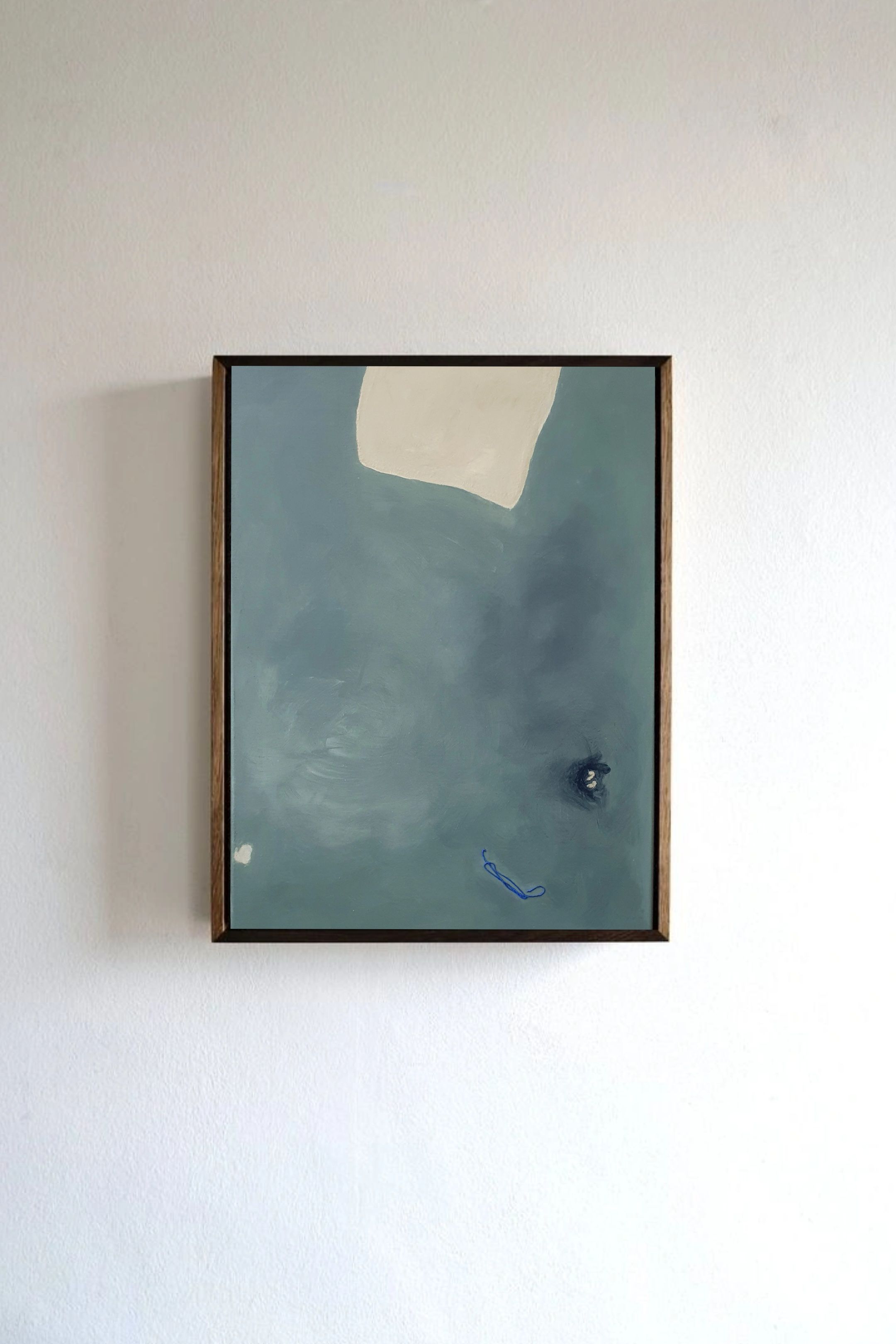 Let go of gravity" by Yeliza Gevorgyan is a minimalist abstract painting framed in wood. It showcases pigments on linen with a large blue-gray area, an off-white shape above, a small dark spot to the right, and a tiny blue mark near the bottom, elegantly set against a plain white wall.