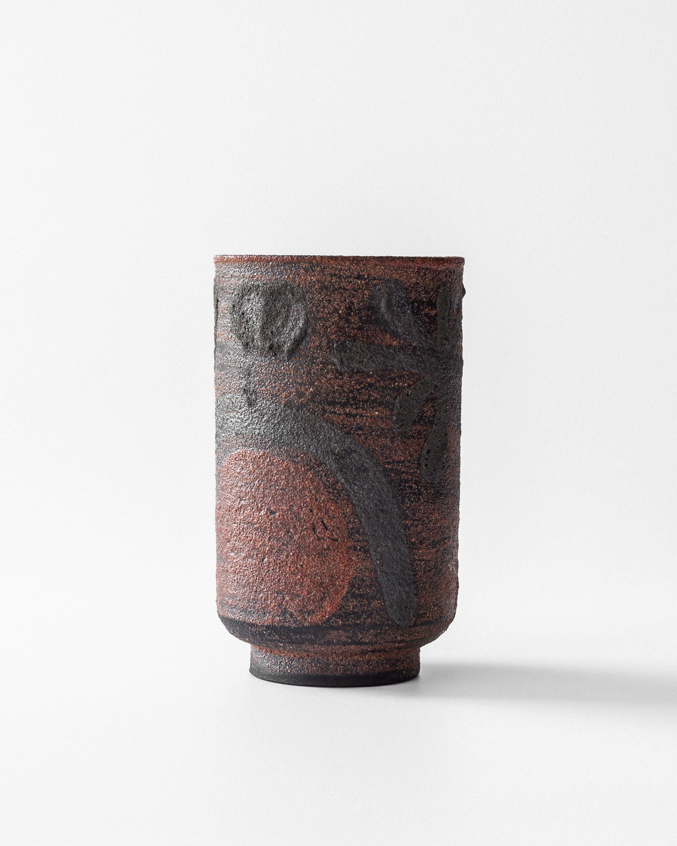 The Modernist Vase by Jaap Dommisse, from Spigel, is a cylindrical ceramic piece featuring earthy browns and deep reds with abstract black patterns. Its textured surface offers an avant-garde appeal when displayed elegantly on a flat surface against a white background.