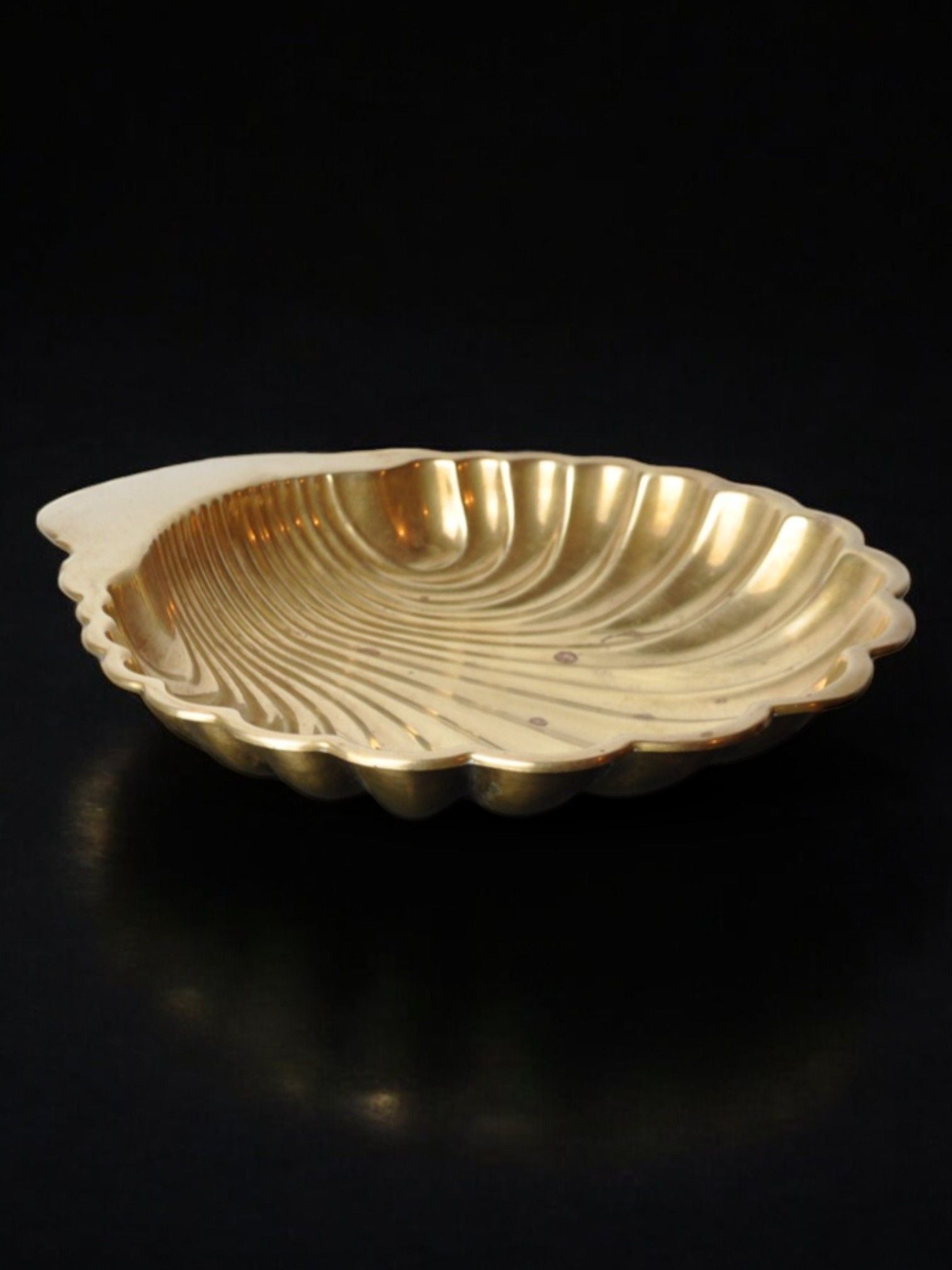 The Large Shell Shaped Vide-Poche 70s by Malamar Studio is a gold dish designed in Italy, featuring a shiny, ribbed scallop shell appearance set against a black background. Its flat rim and intricate brass structure capture the elegance of the ocean's treasures.