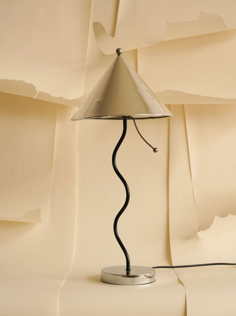 A modern Curly Minimalistic Lamp by Les Objets Amsterdam with a spiral base and conical shade stands against a backdrop of torn beige paper.