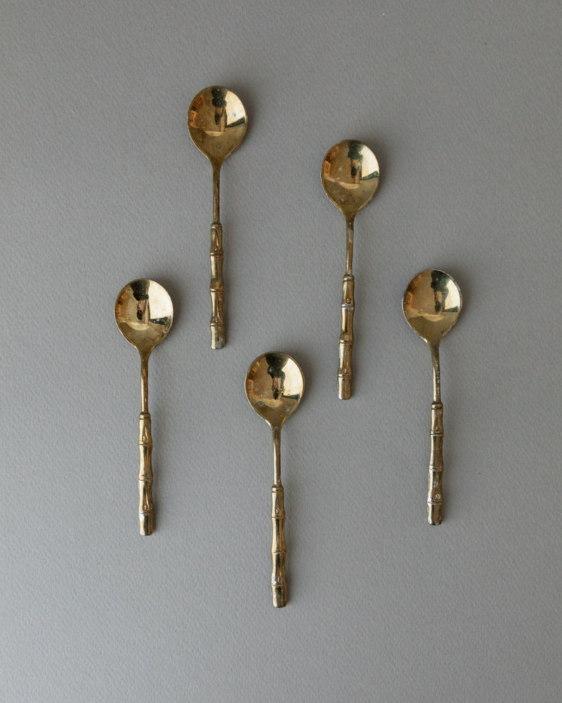 A set of 5 Bottega Jacobs gold-plated teaspoons from the 1970s, featuring round bowls and textured handles in Hollywood Regency style, are evenly arranged on a light gray background.