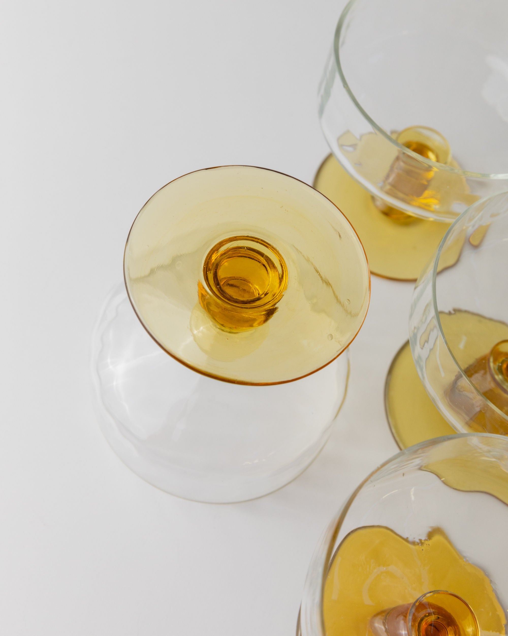 A top-down view shows several Murano glasses with yellow bases from Bottega Jacobs, arranged on a white surface. One glass is upside down, highlighting its yellow base and echoing the mid-century Italian design. This set of 6 captures the essence of Italy in the 70s.