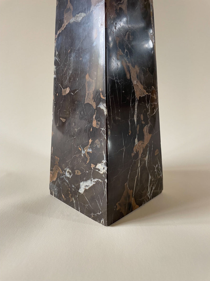 A close-up of the base of a Vintage Marble Obelisk by Maud Vaughan with a polished finish and natural beige veining, standing on a neutral-colored surface. The tall, dark marble object features dark grain and has a tapering, quadrilateral shape.