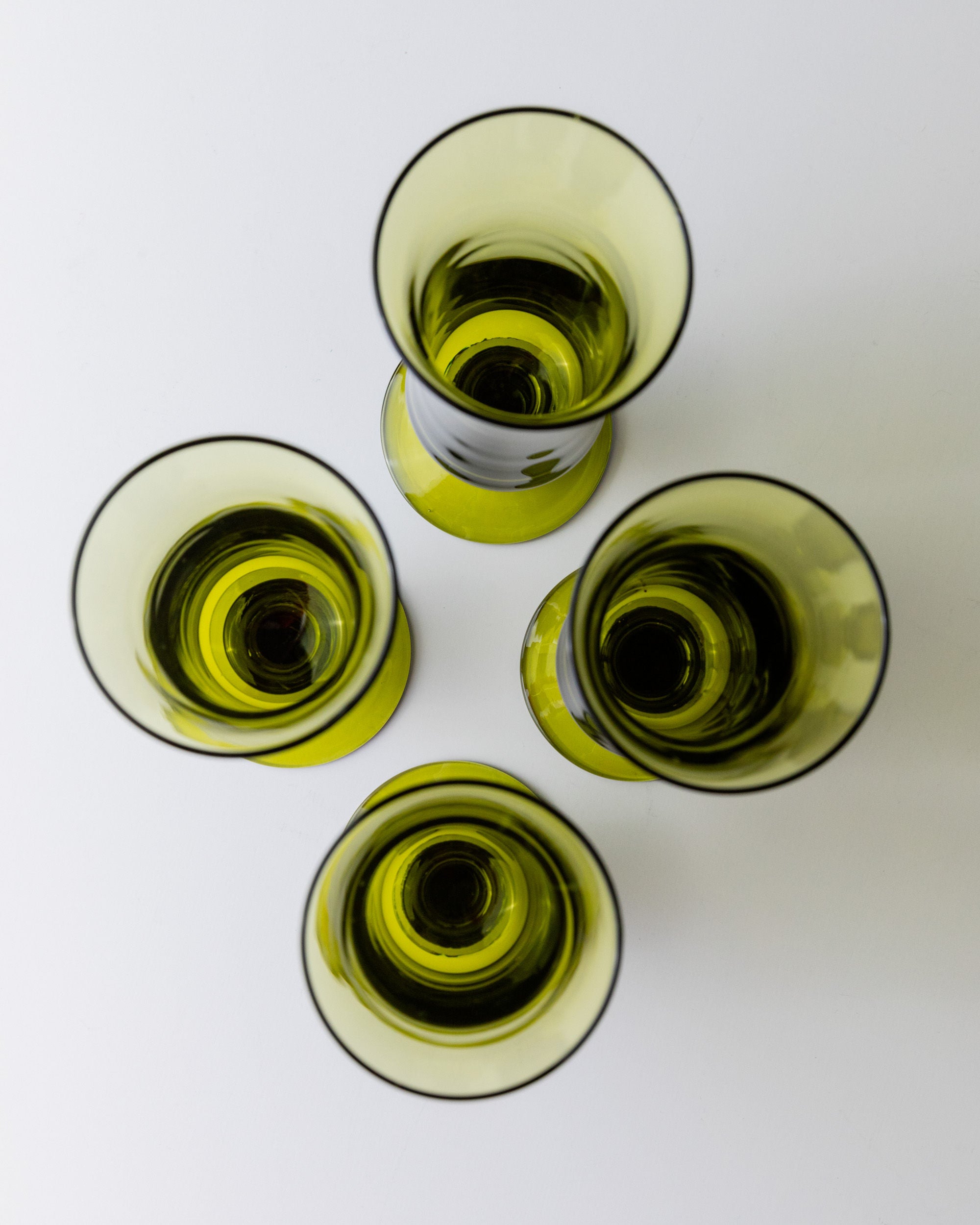 Four "4 Murano Glasses in Green 70s" by Bottega Jacobs are artistically arranged in a circle on a white surface, viewed from above. Their rounded shapes and soft shadows create a symmetrical, abstract pattern that embodies retro chic elegance.