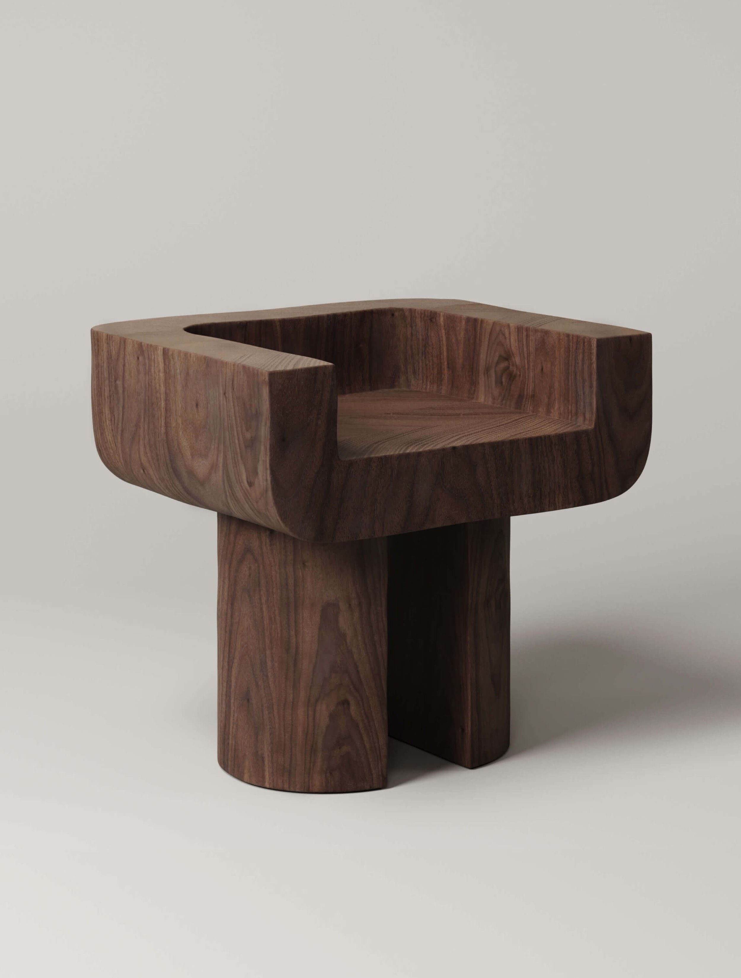 The Monolith M_001 Chair boasts a square design with a carved seat on a solid wood base suitable for indoor/outdoor use. Its smooth finish and central cylindrical leg support enhance the minimalist style against a light gray background.