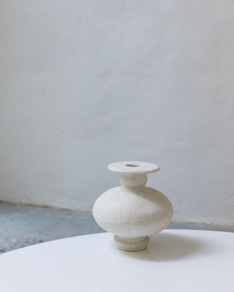 The Calpide Blanco Hueso vase by Canoa Lab features a minimalist, round ceramic form inspired by Mediterranean design, with a matte off-white finish and sculptural shape reminiscent of ancient artifacts.