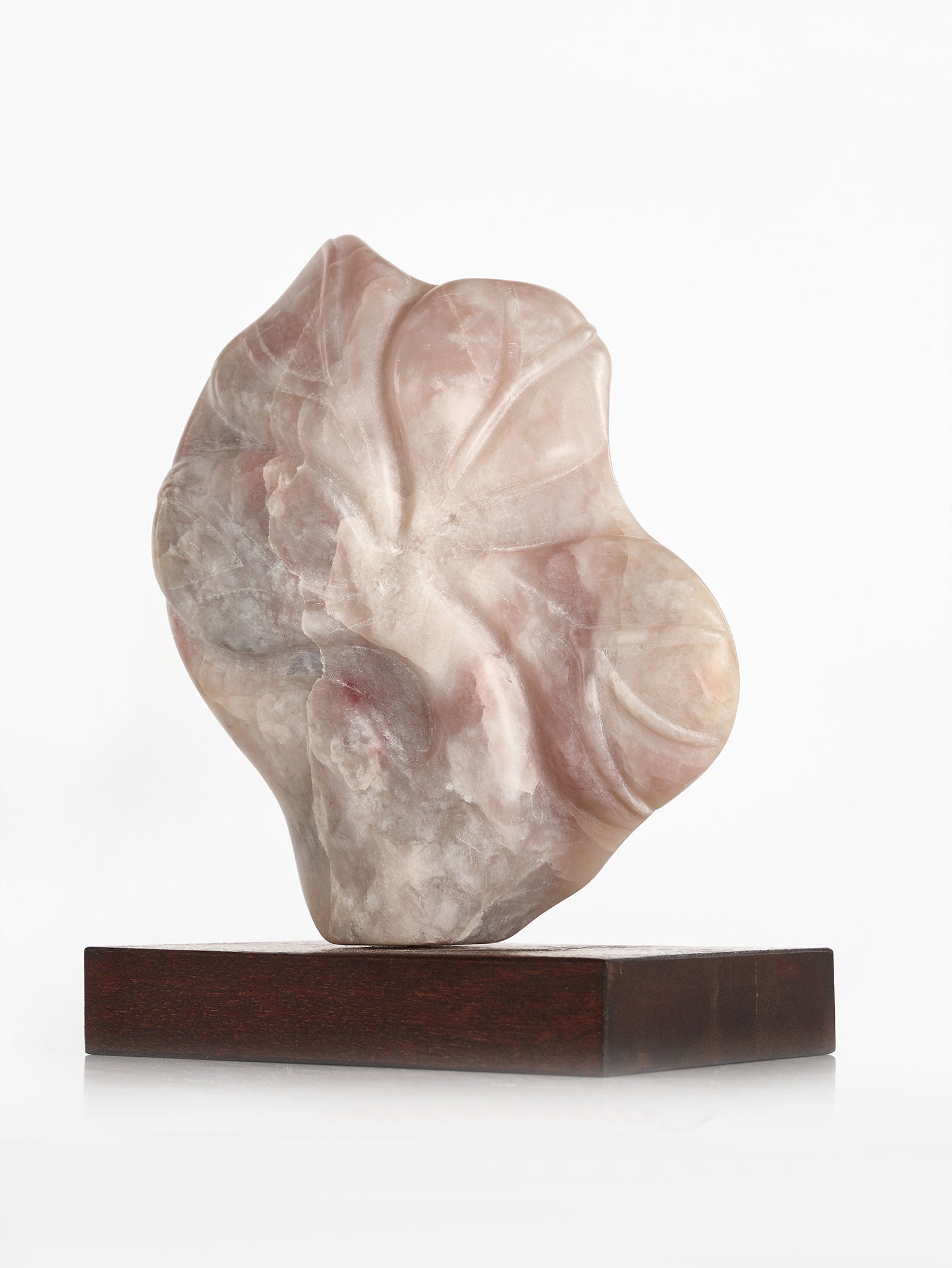 The translucent, abstract stone sculpture "Sculpture by Gisela Peterhof-Heimig," created by RELIC LONDON, showcases soft curves and intricate vein-like patterns reminiscent of a female head. It is elegantly displayed on a dark wooden plinth against a plain white background, creating an enchanting visual contrast.