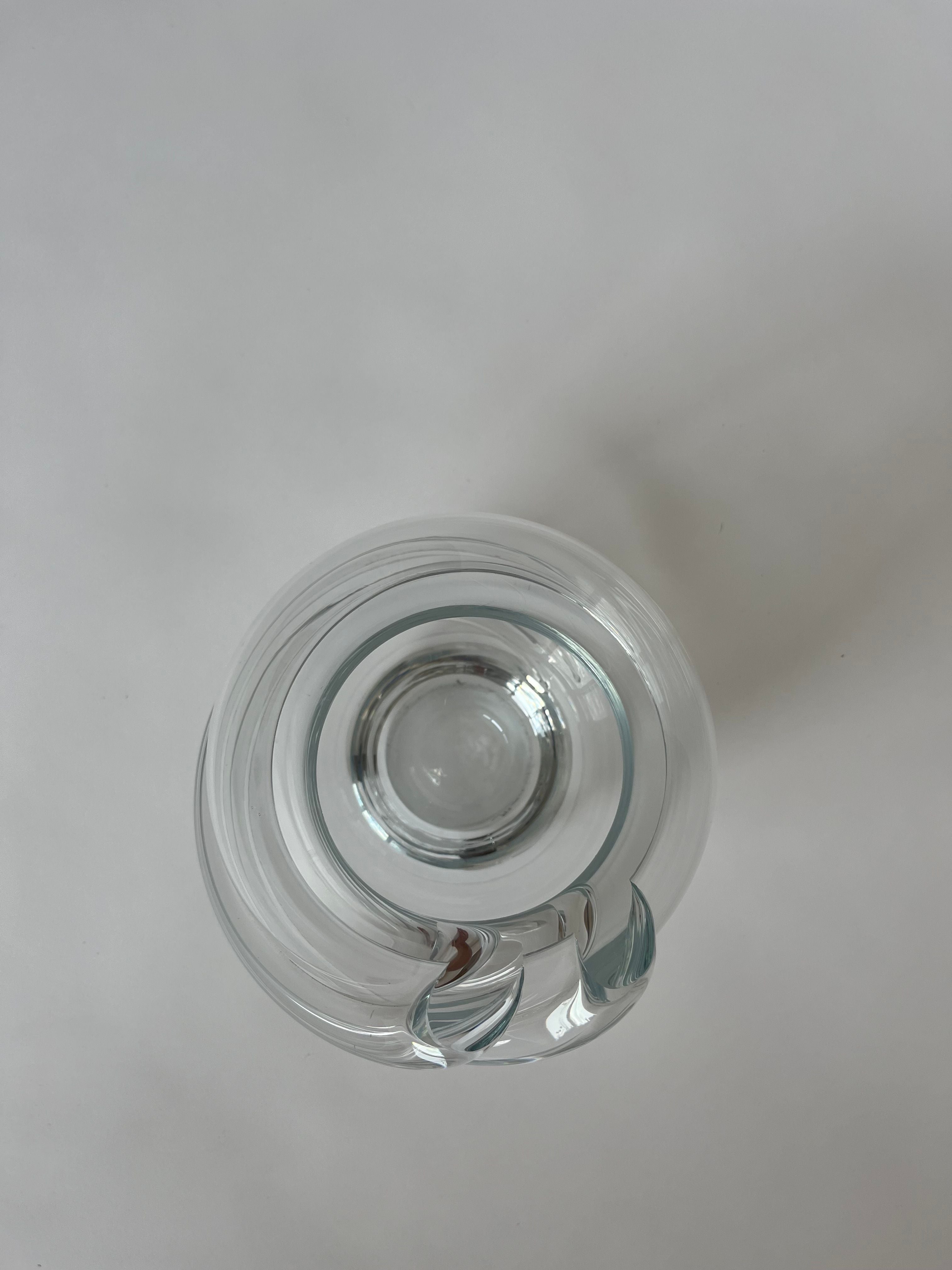 A top view of a Vintage Crystal Vase by septembre studios, featuring a narrow neck and round base, placed on a plain white surface. The glass subtly reflects light, highlighting its transparent and glossy texture, while the elegant swirl details enhance its sophisticated charm.