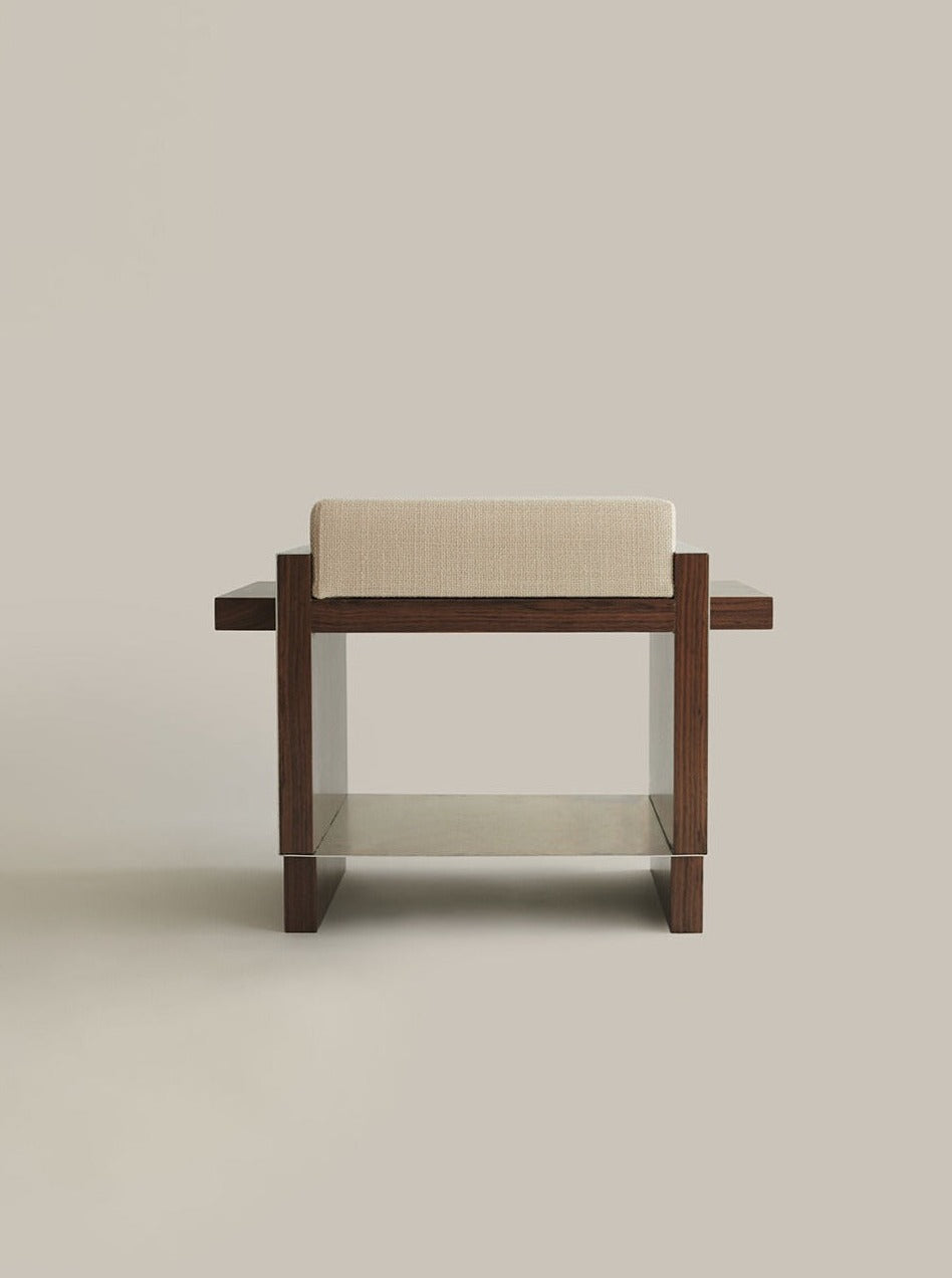 A modern armchair with a minimalist design features a dark walnut wood frame and a light beige cushioned seat. The backrest is also cushioned in the same beige fabric. The chair, branded as B1 [single stool] by Sofia De=Francesco, sits on a neutral, light-colored background.