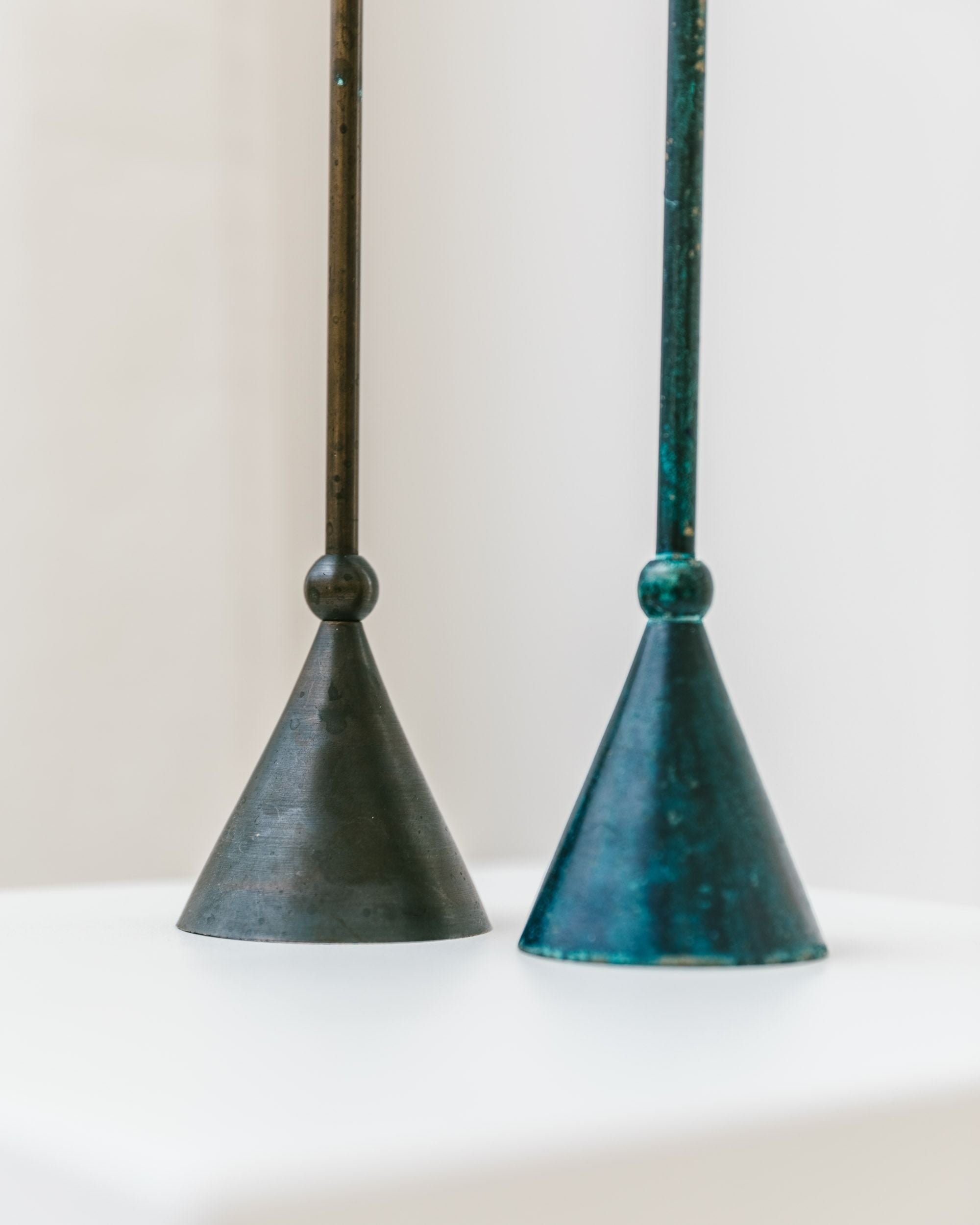 A pair of Postmodern 1980s candleholders from Bottega Jacobs features two conical metal objects with vertical rods extending upwards, each culminating in a spherical knob. The left holder is dark gray, while the right one boasts a bluish-green hue, all set against a light background.