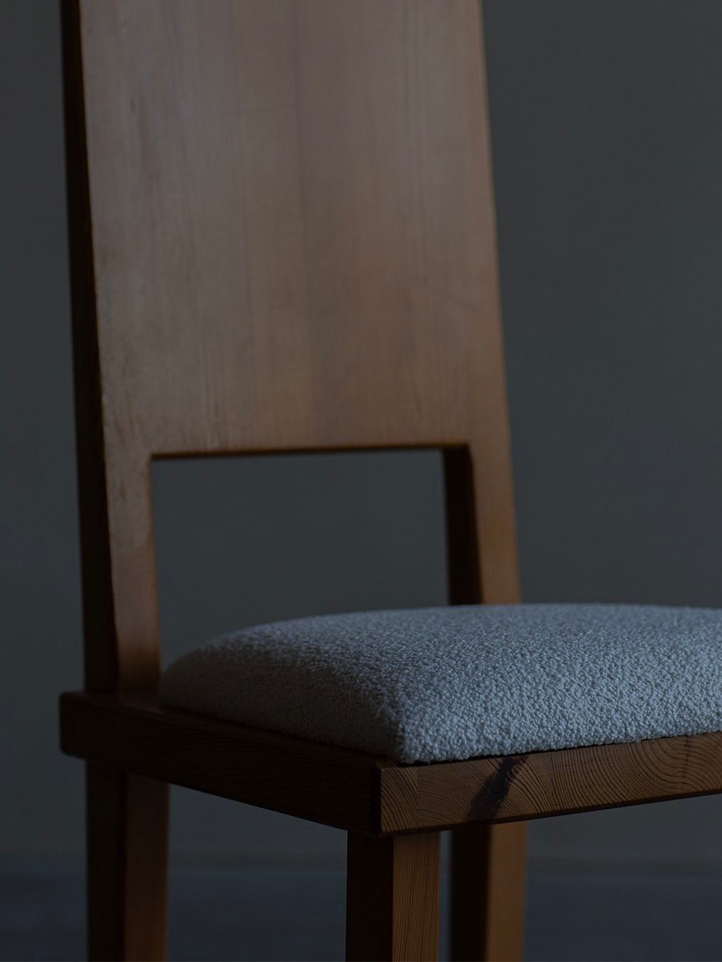 The Göran Malmvall - Model 553 chair by Bicci de' Medici showcases a wooden frame with a tall backrest and a textured light gray cushioned seat. Its simplicity and elegance are highlighted against a dark background, exemplifying Swedish furniture design.