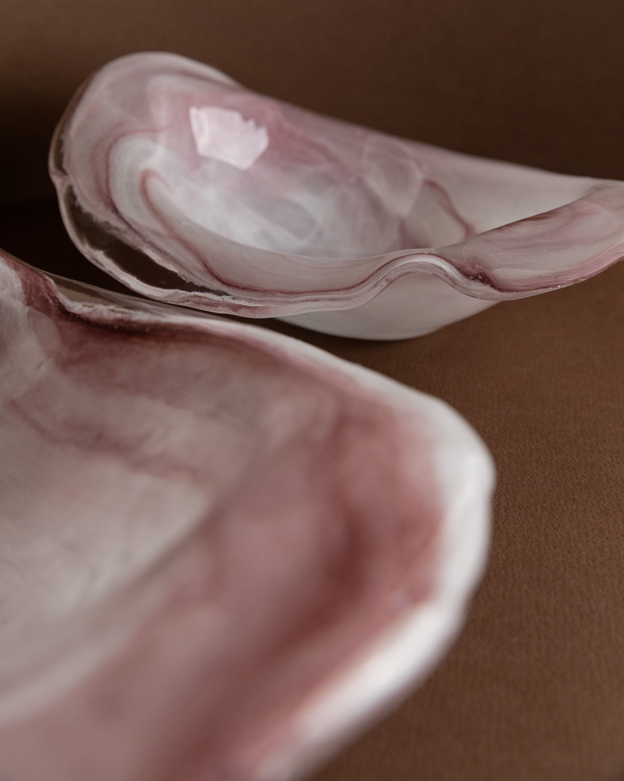 Two Murano Glass Bowls by Bottega Jacobs, Italy 1970s, featuring organic wavy edges and marbled pink and white patterns, are displayed on a brown surface, highlighting their smooth texture and vintage style.