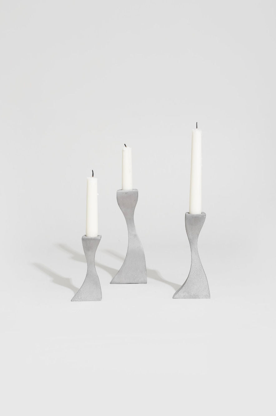 The Villa Wavy Candleholder Set features three modern metal holders of varying heights, each with a wavy design and displaying an unlit white taper candle against a plain white background.
